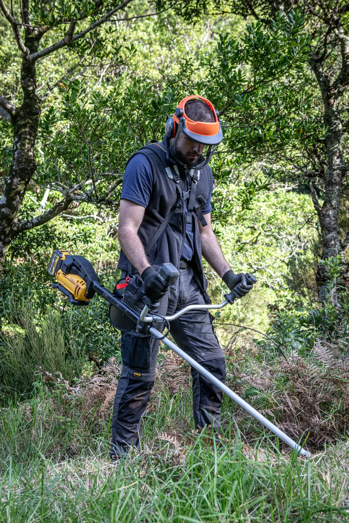 Person uses DEWALT DCMBC823N, DCMBC823N-XJ brushcutter outdoors. Protective gear visible. Photography category.