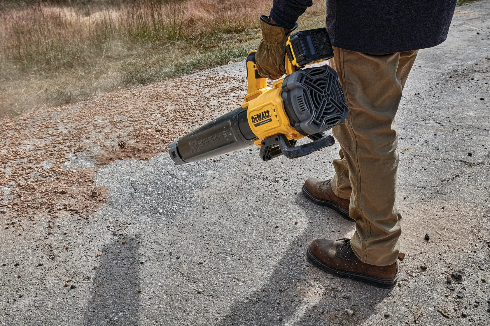 Persona usa un soplador inalámbrico DEWALT para limpiar residuos de una superficie exterior pavimentada.