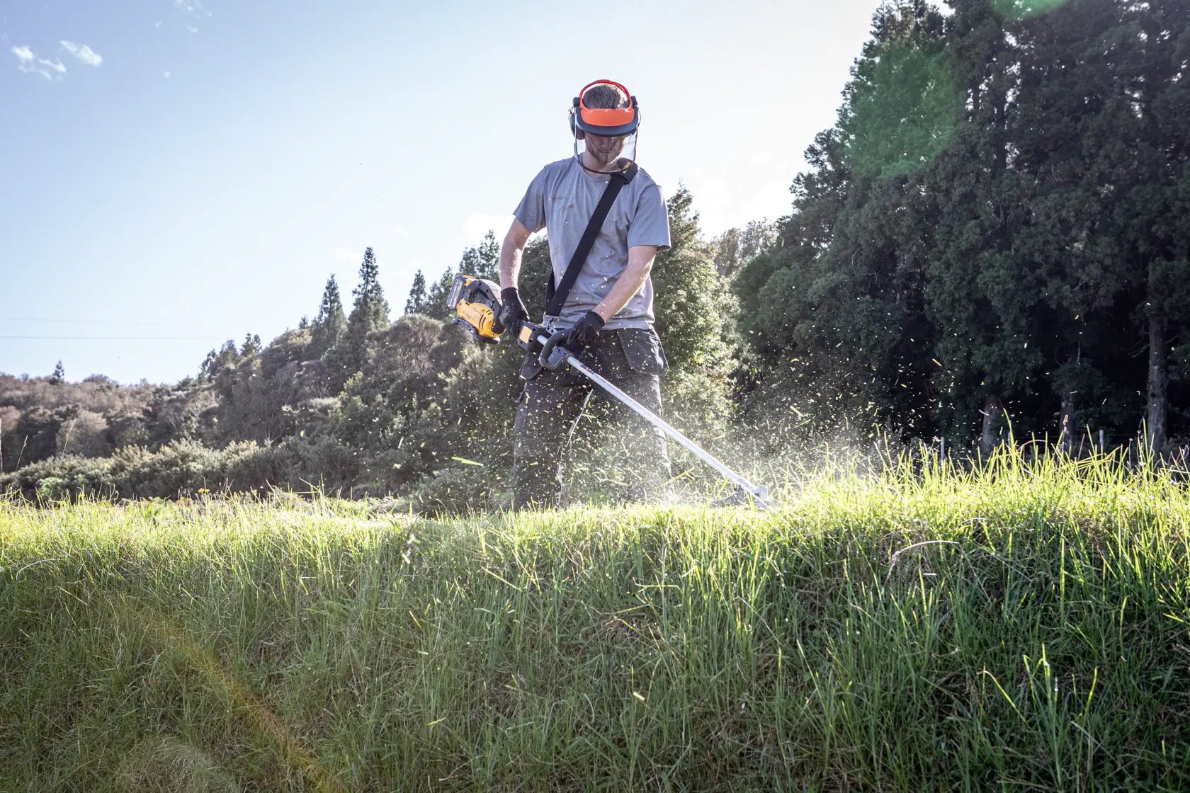 Person trims grass with DEWALT DCMST911N, DCMST911N-XJ. Outdoor, safety gear, photography category.