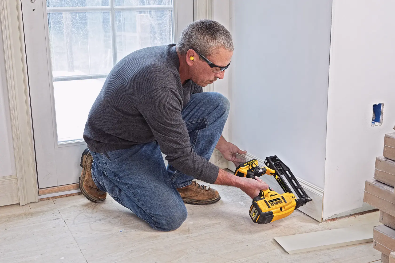 Person using a DEWALT cordless nailer to install baseboards near a door in a room under renovation.