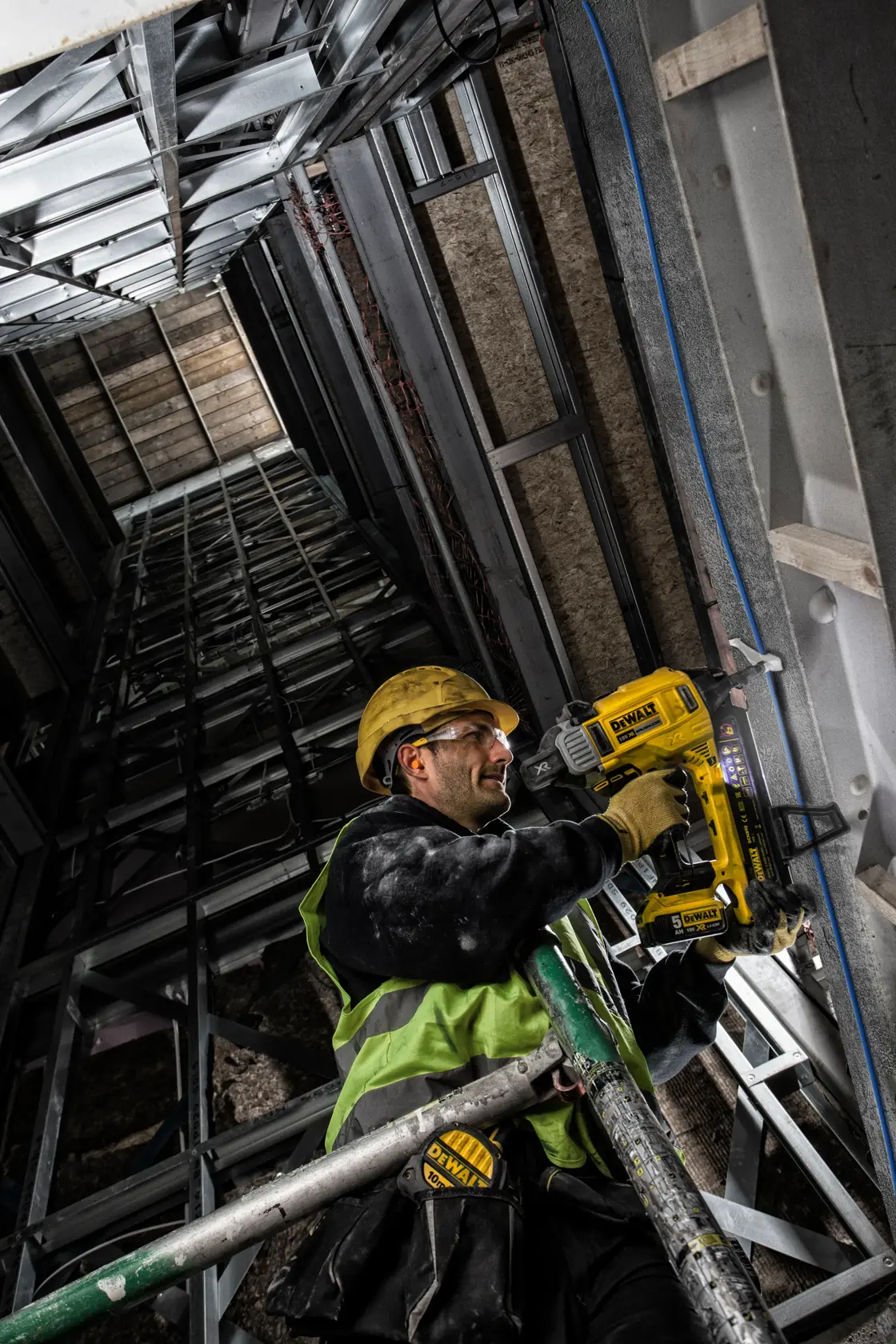 Trabajador usa clavadora DEWALT DCN890P2 en estructura metálica, lleva equipo de seguridad.