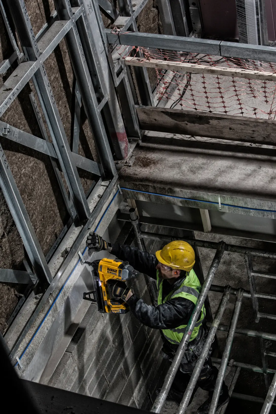 Trabajador usa clavadora DEWALT DCN890P2 en el marco de pared, con equipo de seguridad en obra.