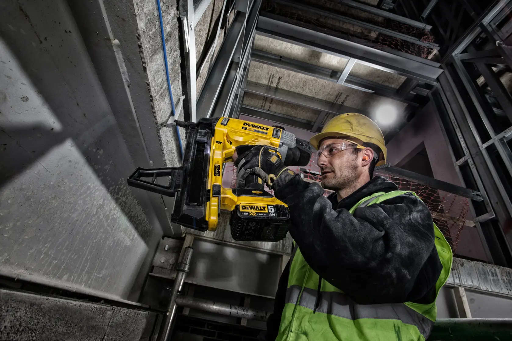 Trabajador usa DEWALT DCN890P2 clavadora en estructura metálica, lleva casco y ropa de seguridad.