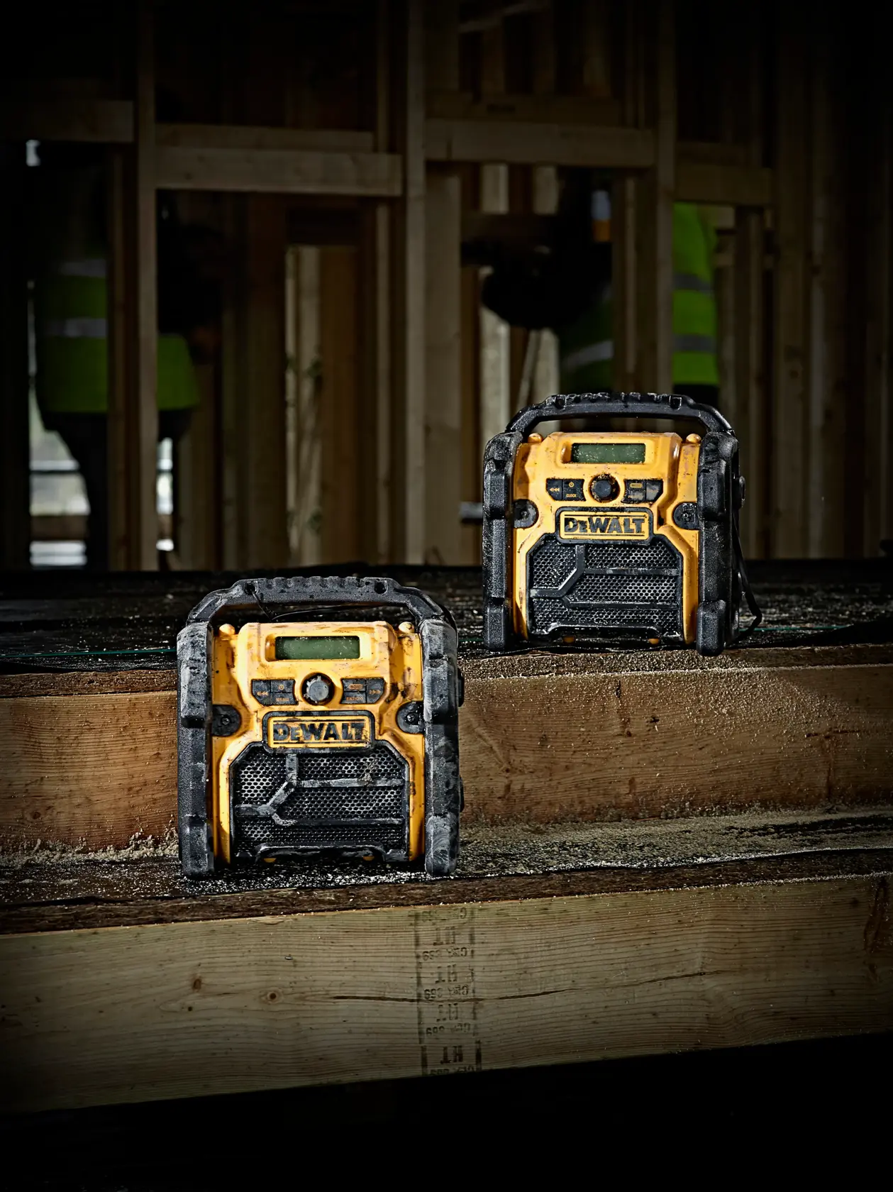 Dos radios DEWALT DCR019 sobre banco de madera en obra con estructura de madera sin terminar.