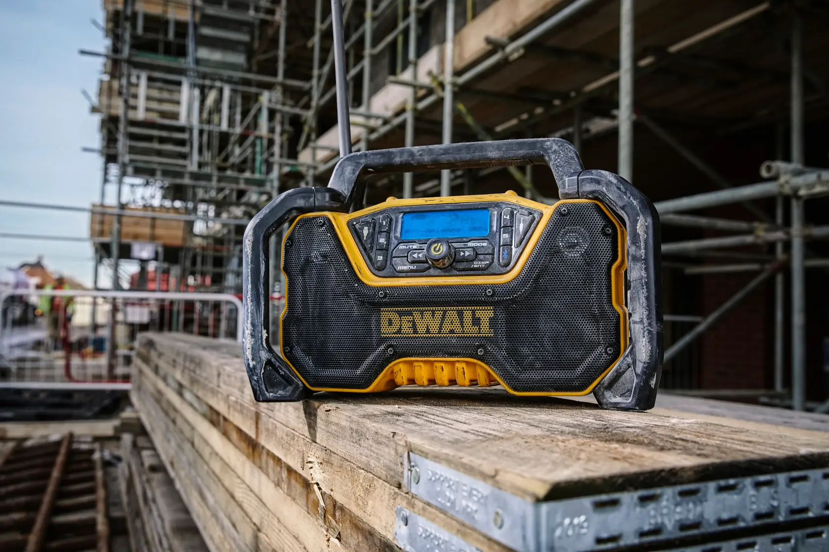 DEWALT Baustellenradio auf Holzplanken an einer Baustelle, umgeben von Gerüsten und Baumaterialien.