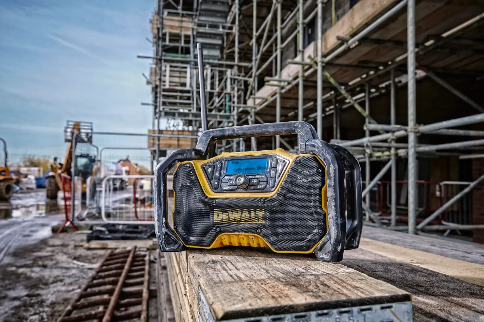 DEWALT tragbares Radio auf Holzplanken an einer Baustelle, umgeben von Gerüst und Geräten.