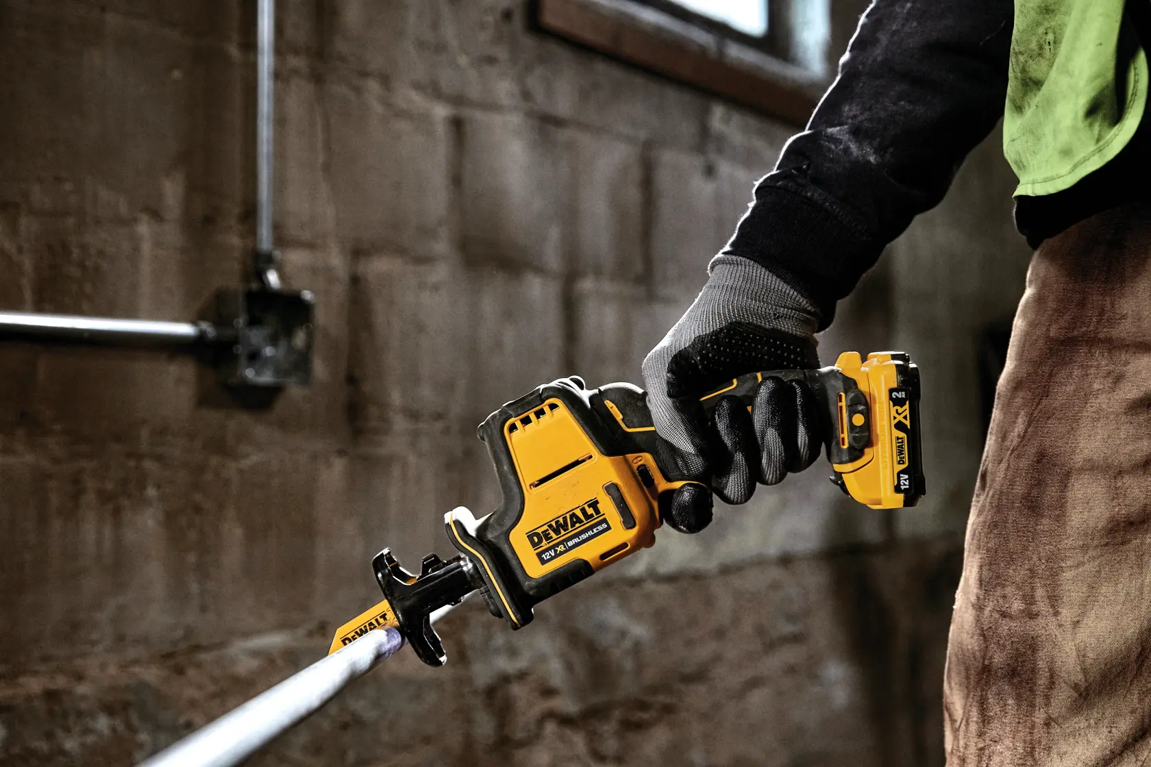 Mano enguantada sostiene sierra recíproca DEWALT DCS312D2 cortando tubo metálico en interior.