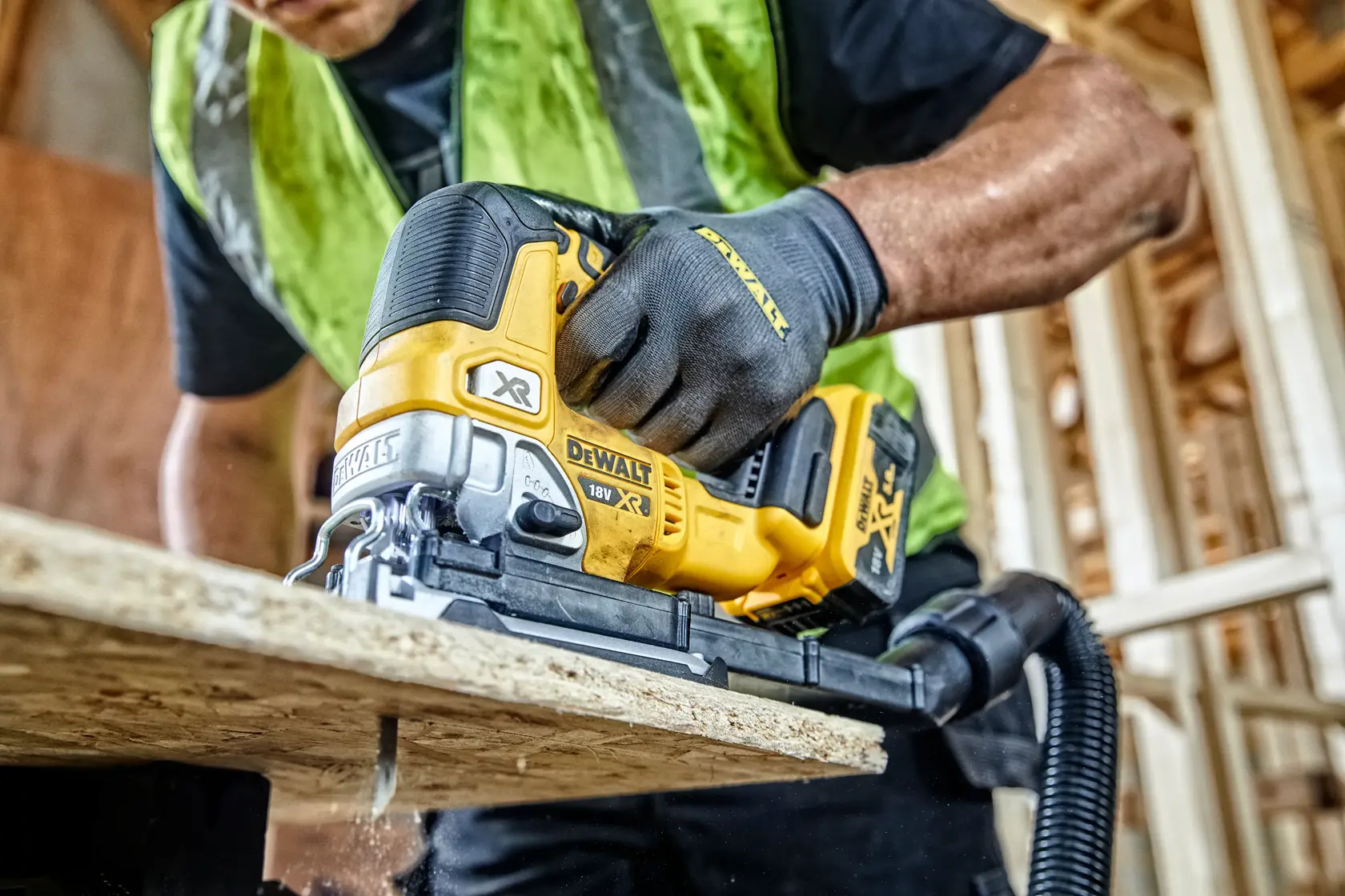 DEWALT cordless jigsaw cutting wood at a construction site, held by a worker in safety gear.