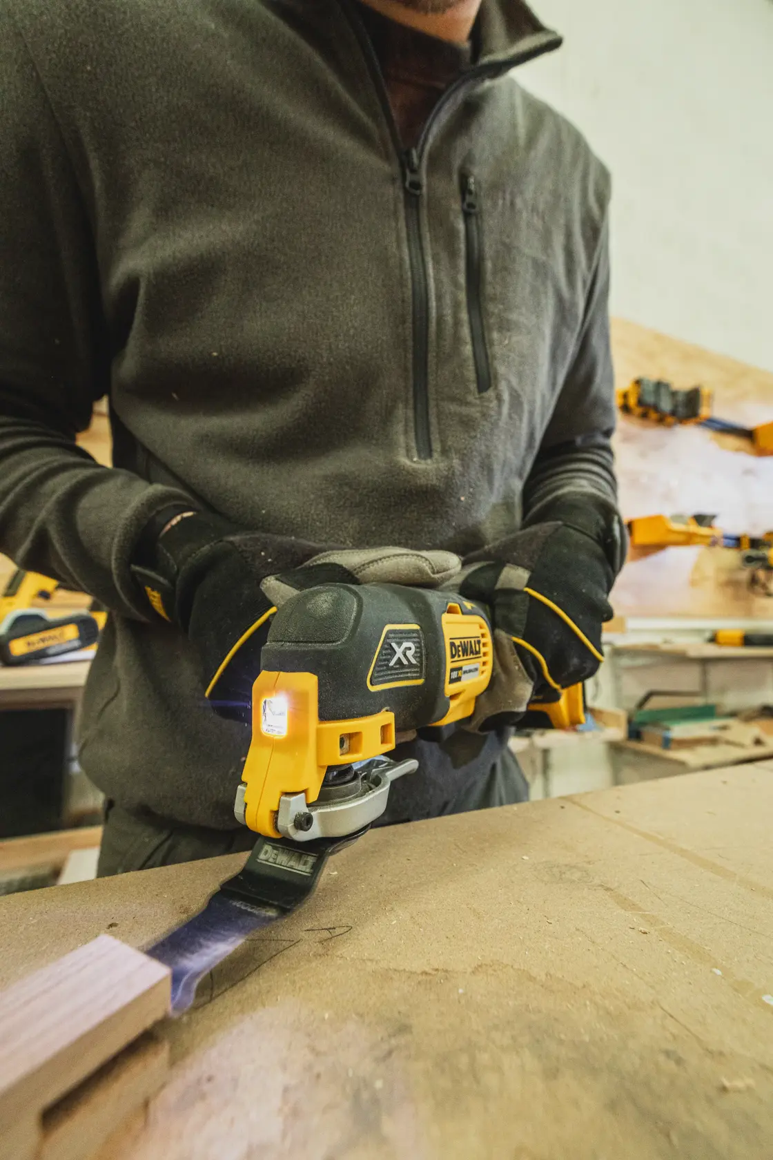 Person uses a DEWALT DCS355N-XJ oscillating multi-tool to cut wood in a workshop.