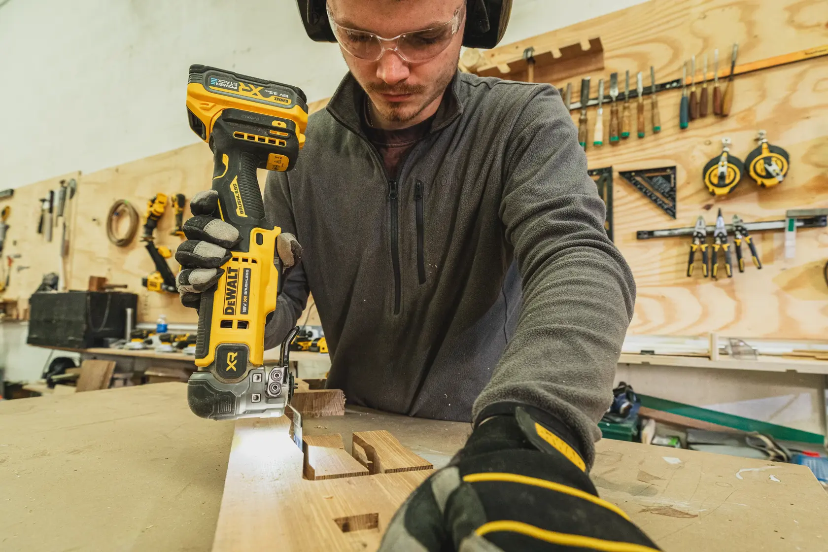 Person uses a DEWALT DCS359N-XJ cordless saw to cut wood on a workbench in a workshop.