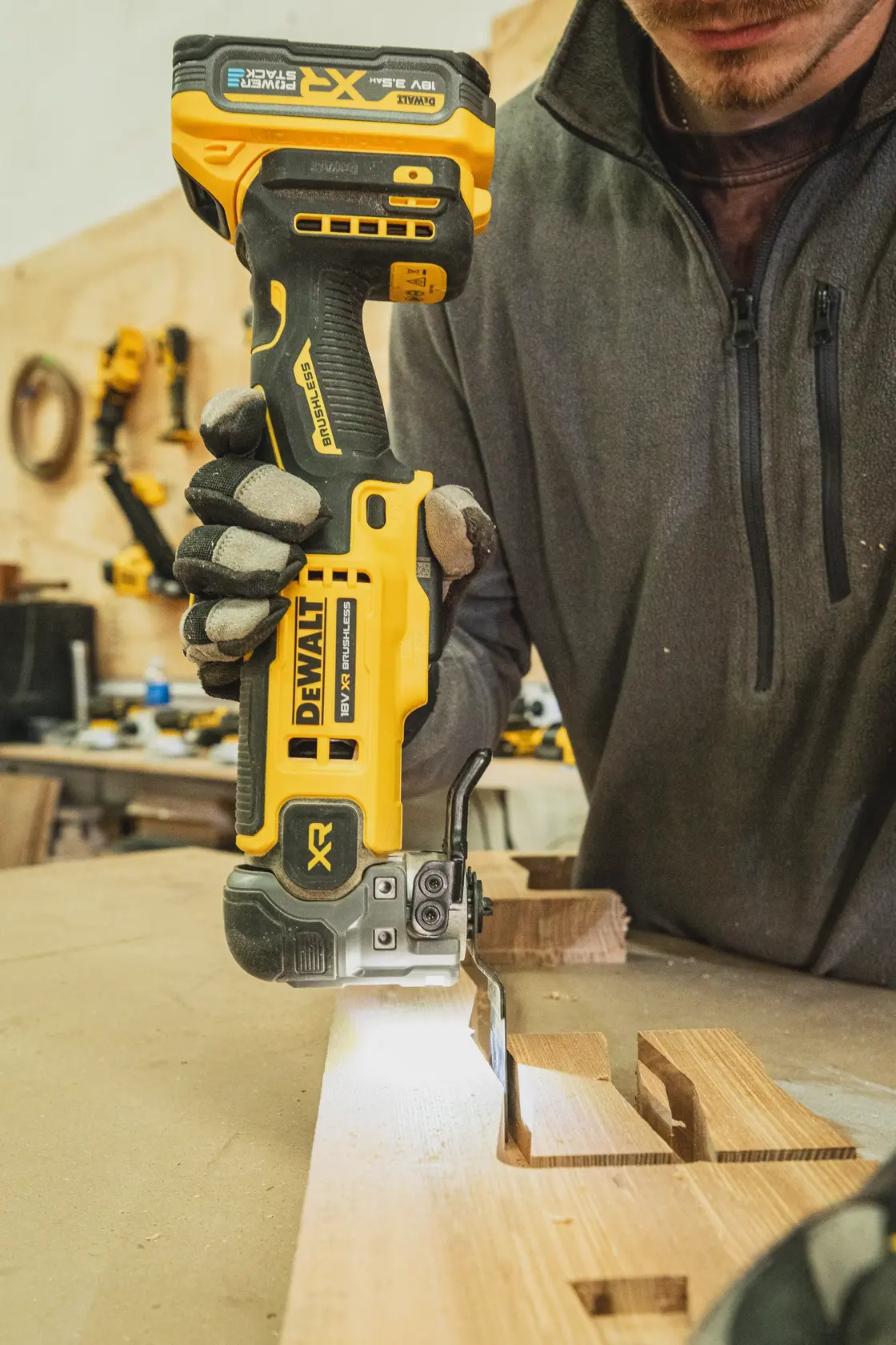 Person using DEWALT cordless jigsaw to cut wood on a workbench in a workshop.