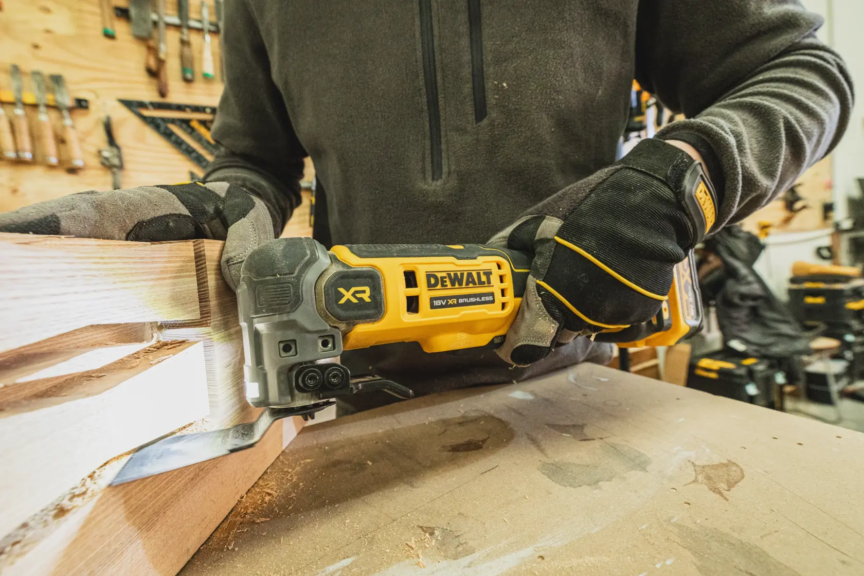 Person using a DEWALT XR brushless power tool to cut wood in a workshop, wearing gloves and workwear.