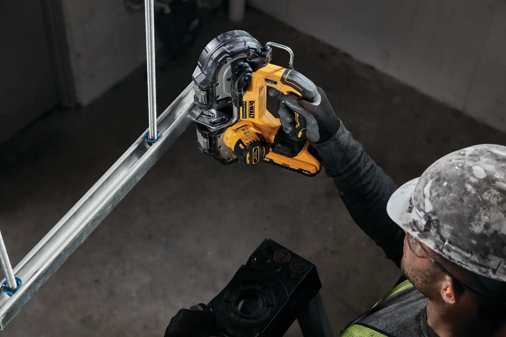 Trabajador corta tubo de metal con sierra de banda inalámbrica DEWALT amarilla.