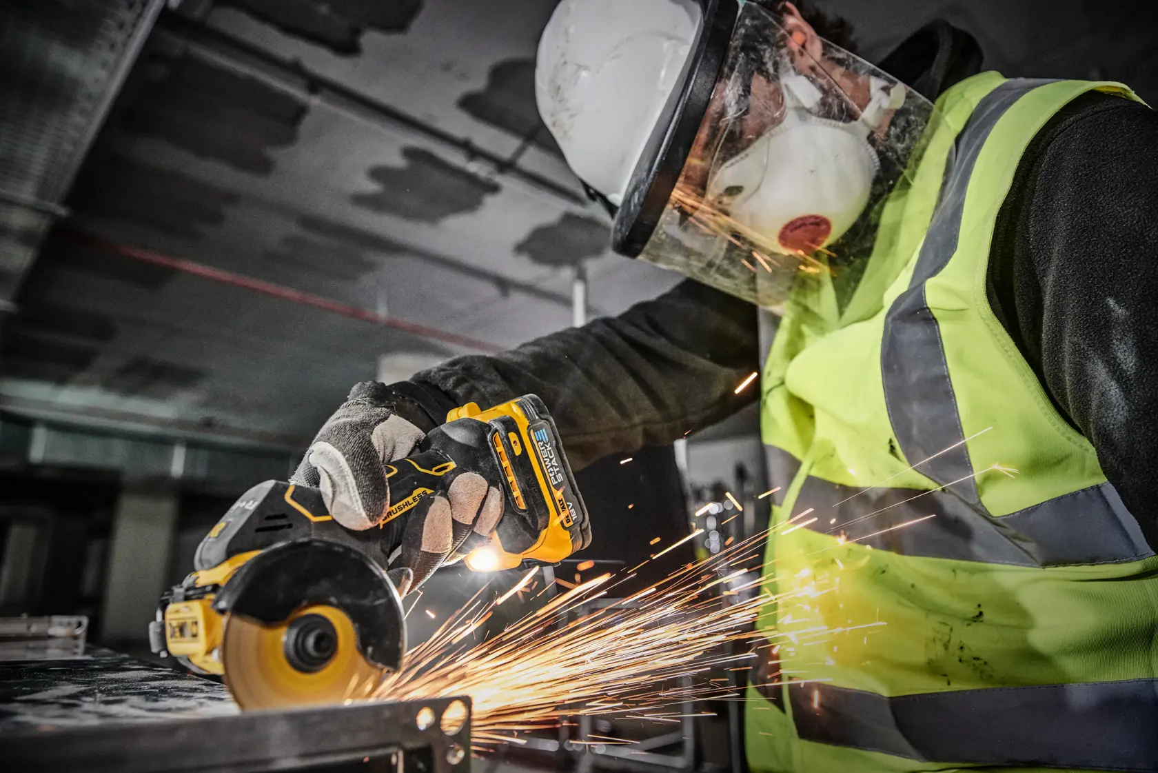 Una persona con equipo de seguridad, incluyendo casco, pantalla facial, mascarilla, guantes y chaleco de alta visibilidad, utiliza una herramienta eléctrica inalámbrica DEWALT DCS438N para cortar metal, produciendo chispas.
