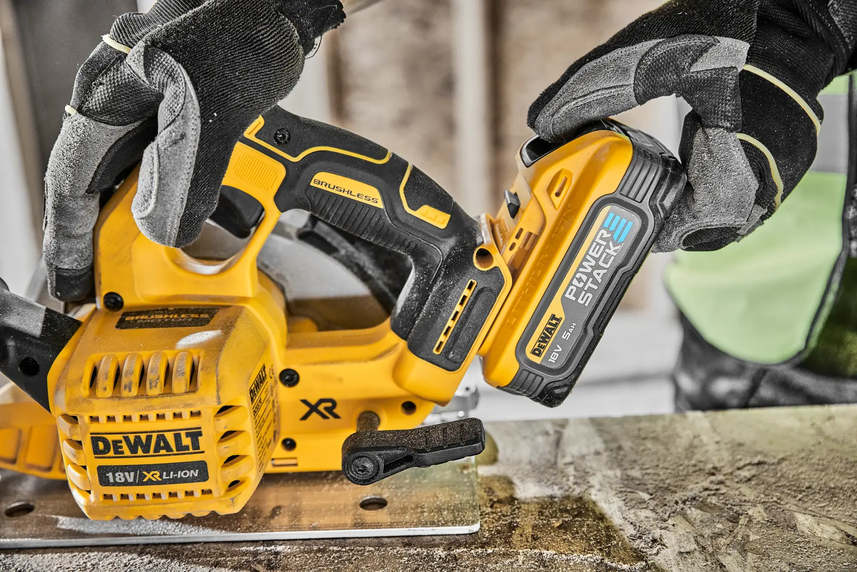Gloved hands attach a DEWALT 18V battery to a yellow cordless saw on a workbench.