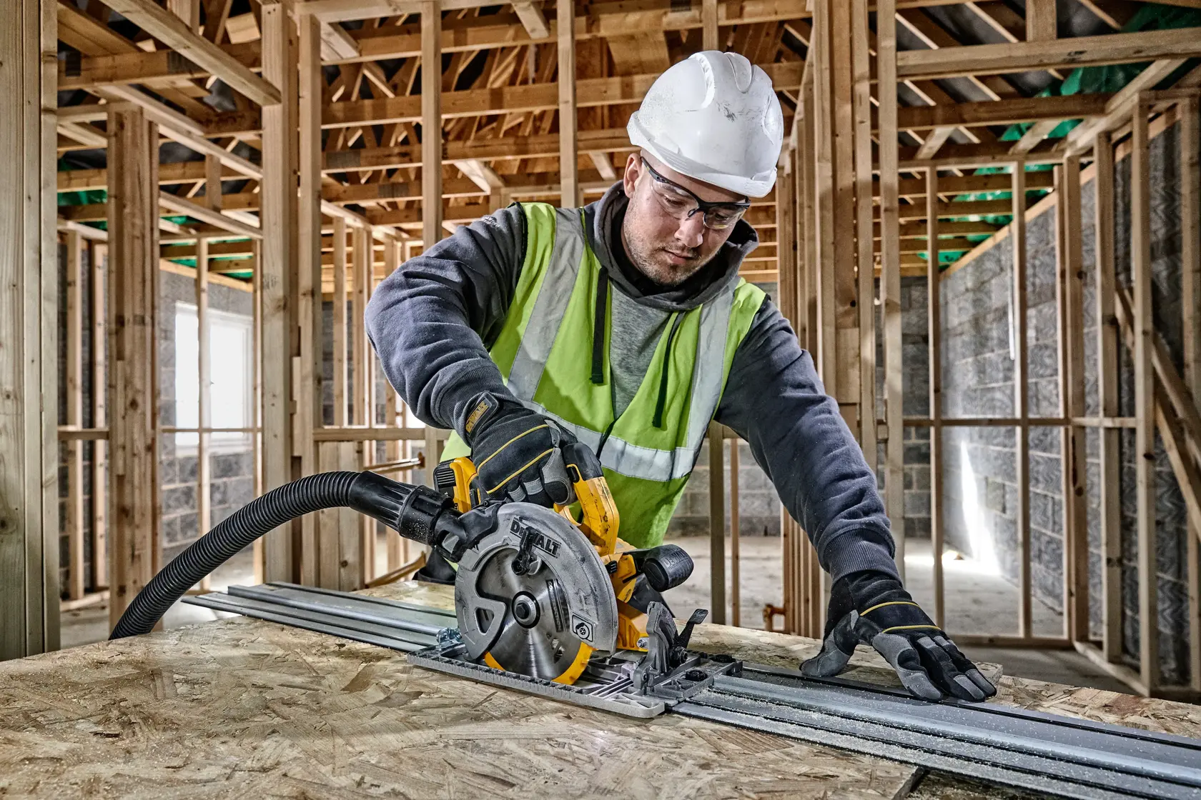 Worker uses a DEWALT circular saw to cut wood in a building under construction. Safety gear is worn.