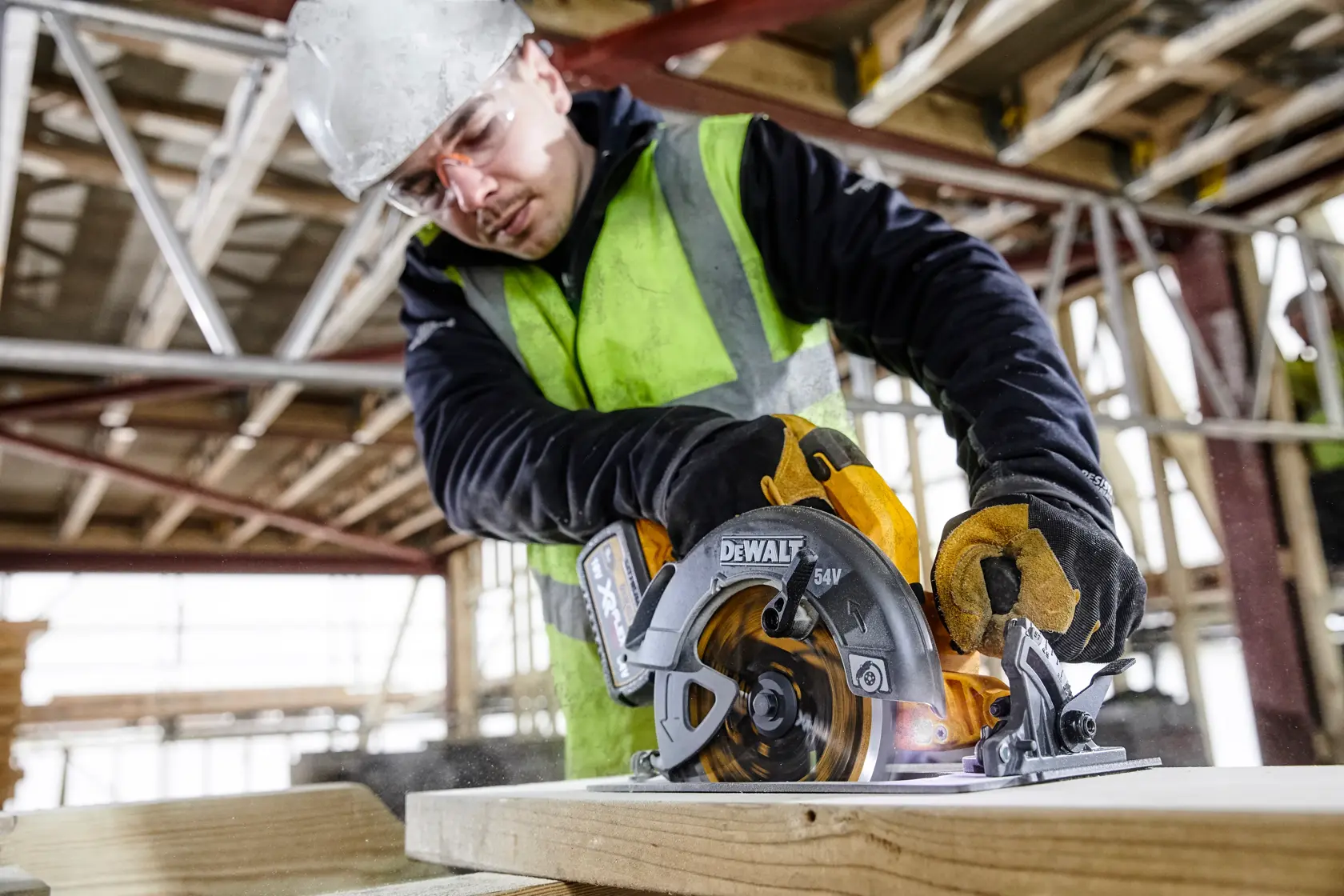 DEWALT Akku-Kreissäge schneidet Holz, gehalten von Handschuhen auf einer Baustelle.