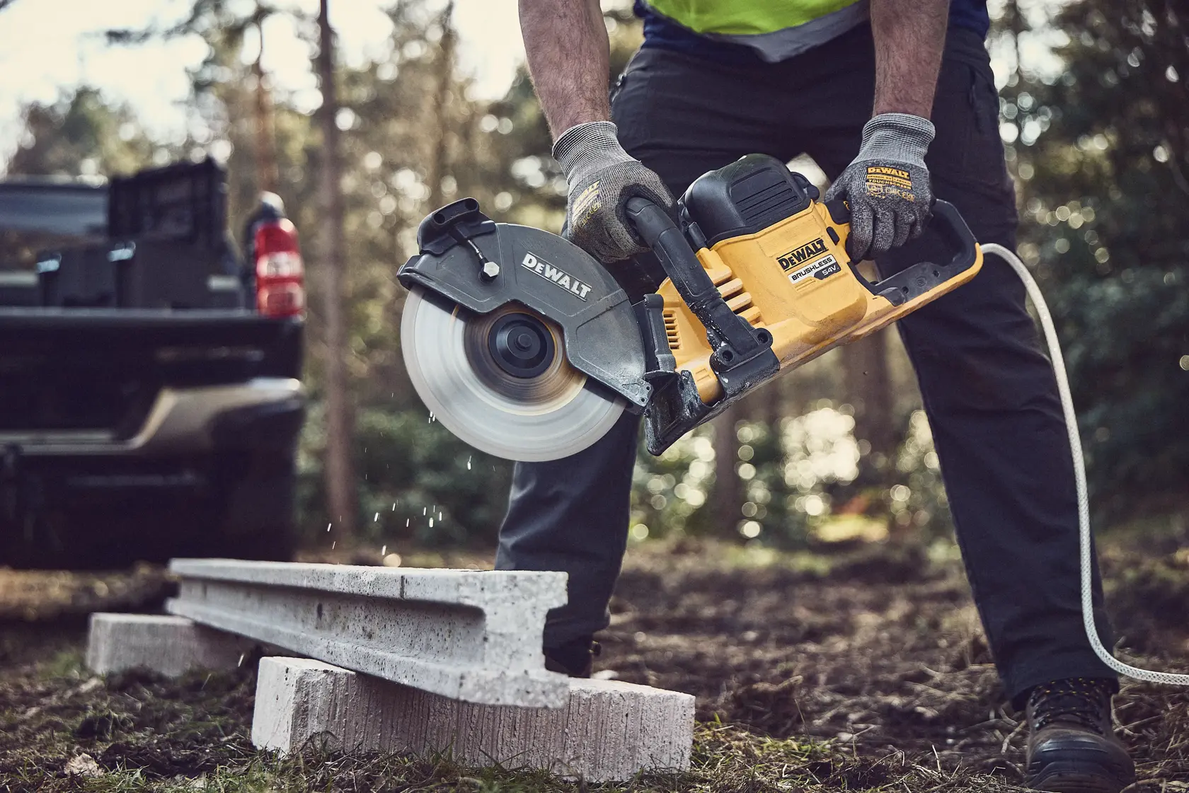 Persona cortando concreto al aire libre con sierra DEWALT DCS691X2 y guantes de seguridad.