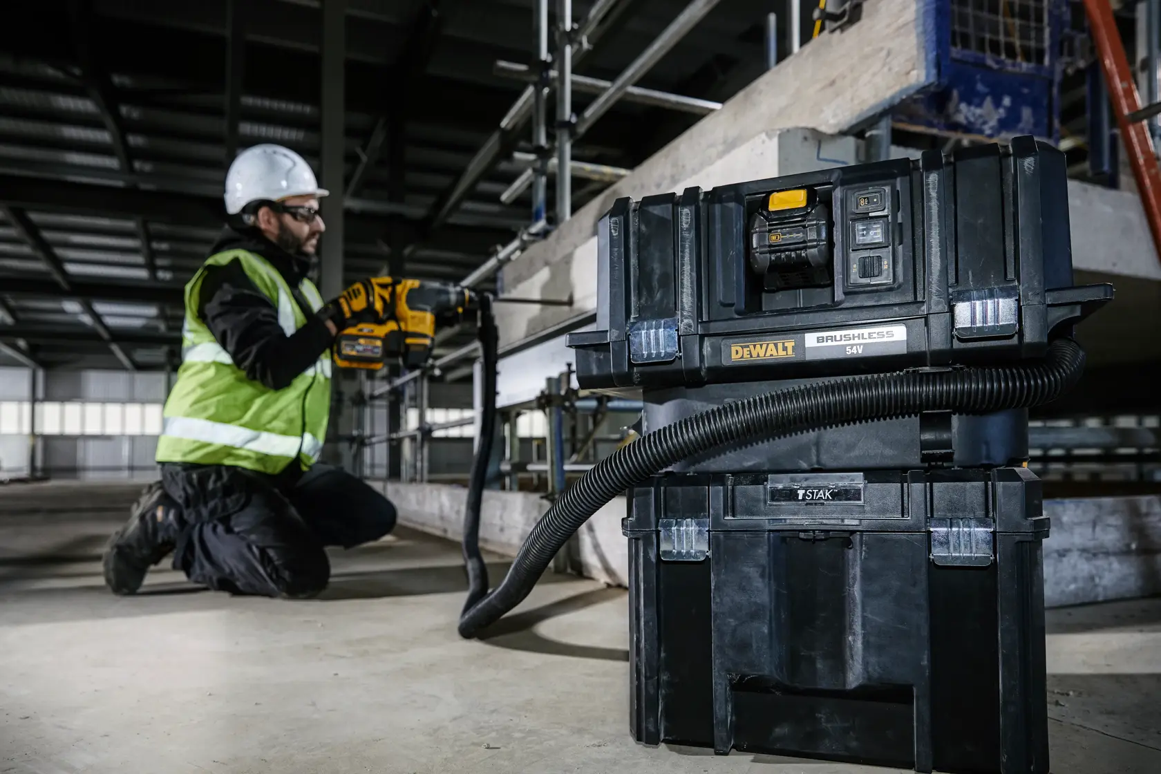 Aspiradora DEWALT DCV586MT2 en obra, conectada a herramienta manejada por trabajador con equipo de seguridad.