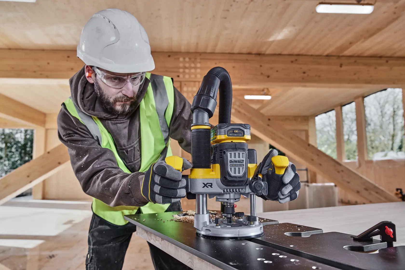 Arbeiter nutzt DEWALT XR DCW620H2 Fräse auf einer Platte, trägt Schutzkleidung.