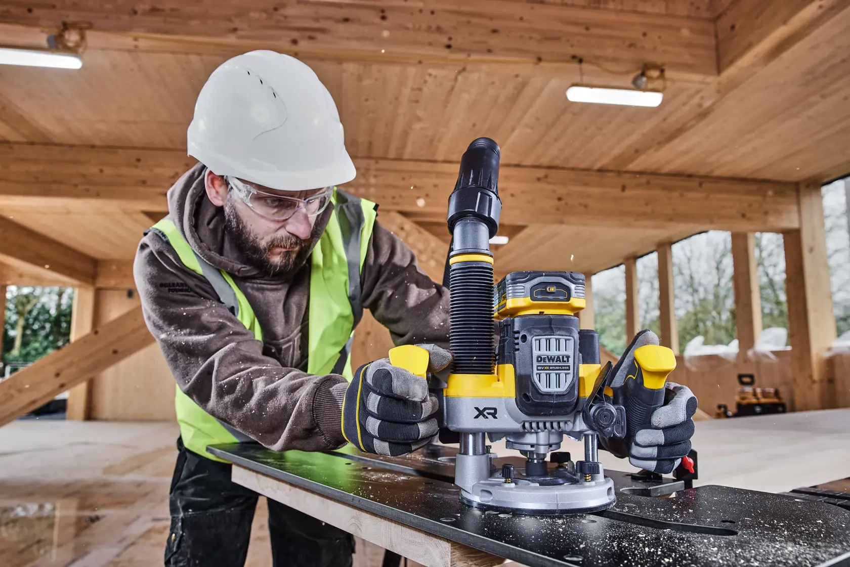 Arbeiter nutzt DEWALT DCW620H2 Fräse auf Holz in Baustelle, mit Sicherheitskleidung und Handschuhen.