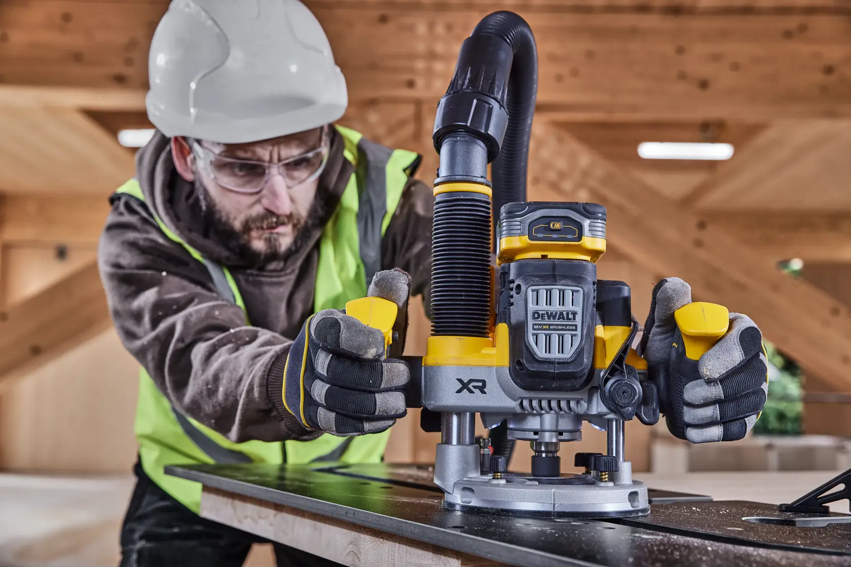 Trabajador usa una fresadora DEWALT XR sobre madera, con equipo de seguridad, en obra interior.