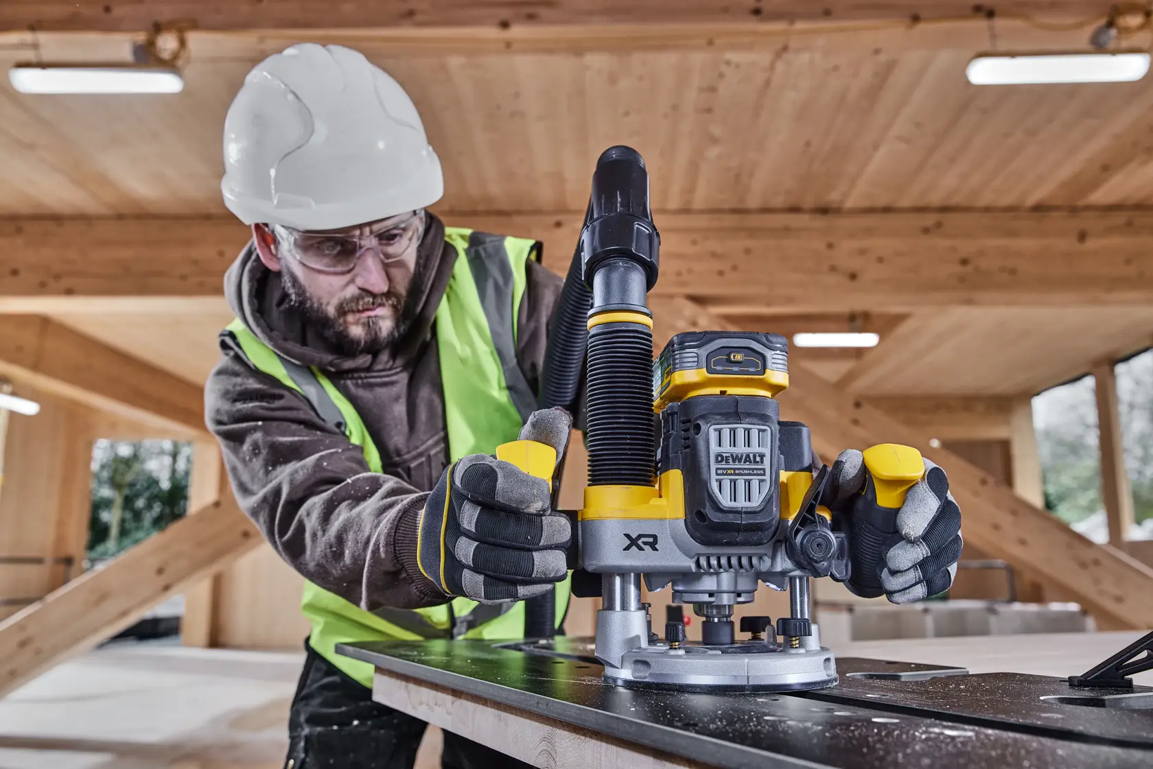 Trabajador utiliza la fresadora DEWALT DCW620NT en madera, con guantes, chaleco y casco.