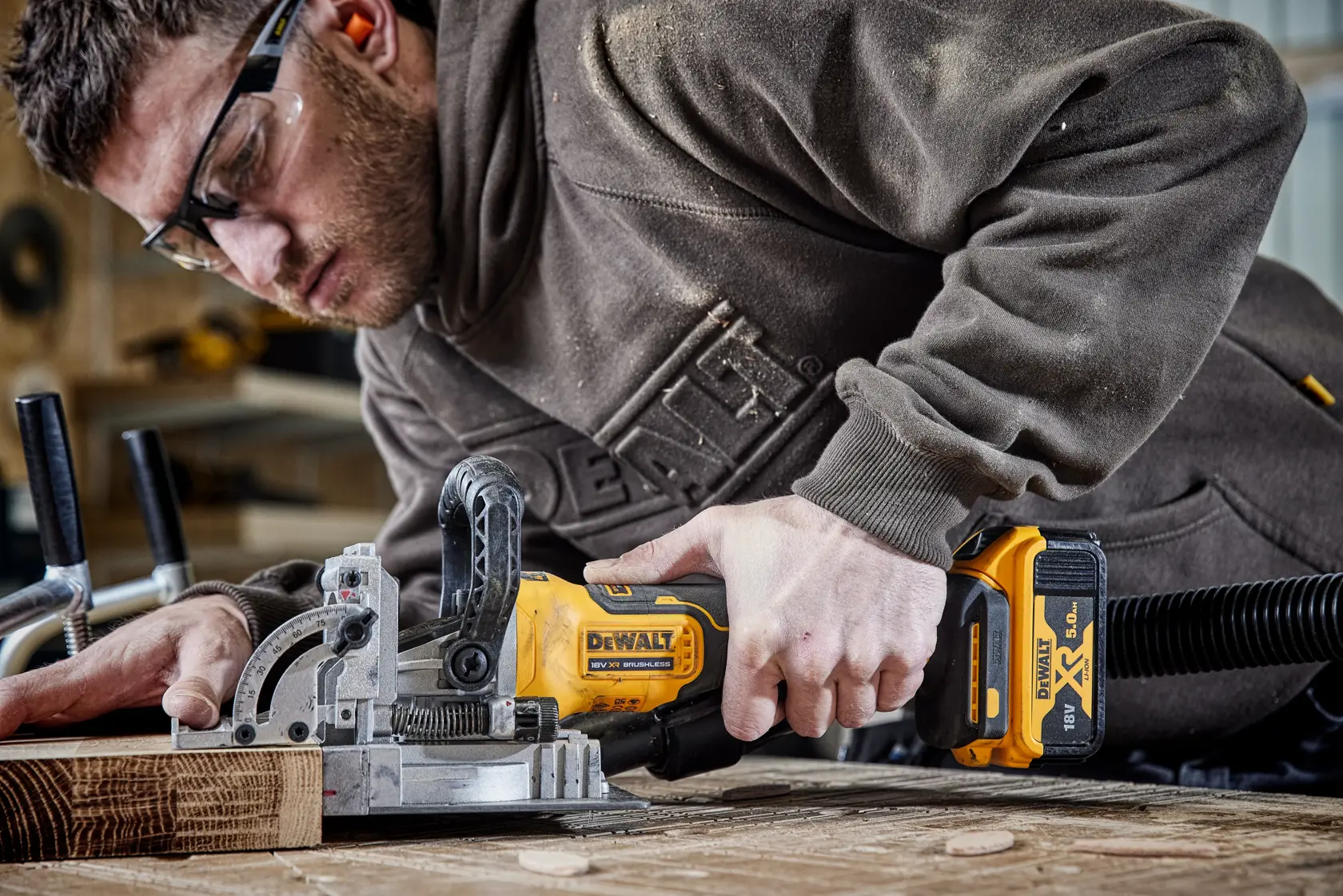 Person using a DEWALT DCW682N cordless biscuit joiner on a wooden workpiece, workshop setting.