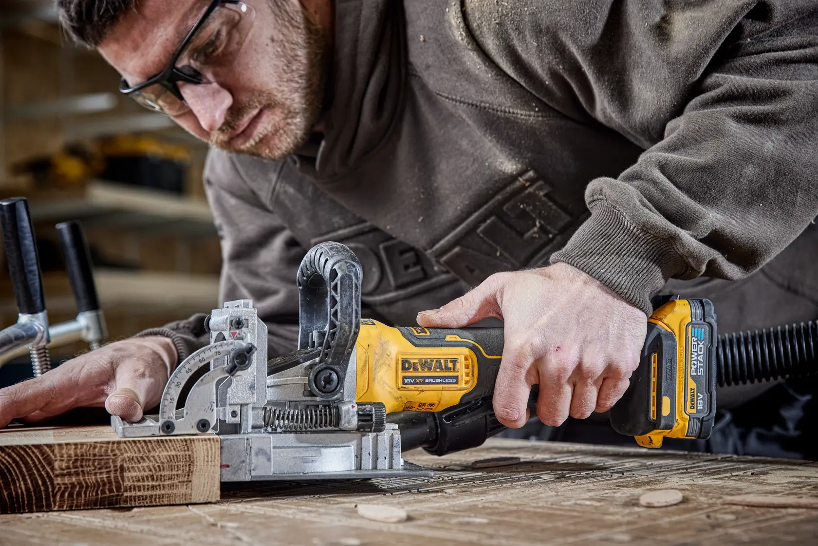 Person using a DEWALT DCW682N cordless joiner tool to work on wood in a workshop setting.