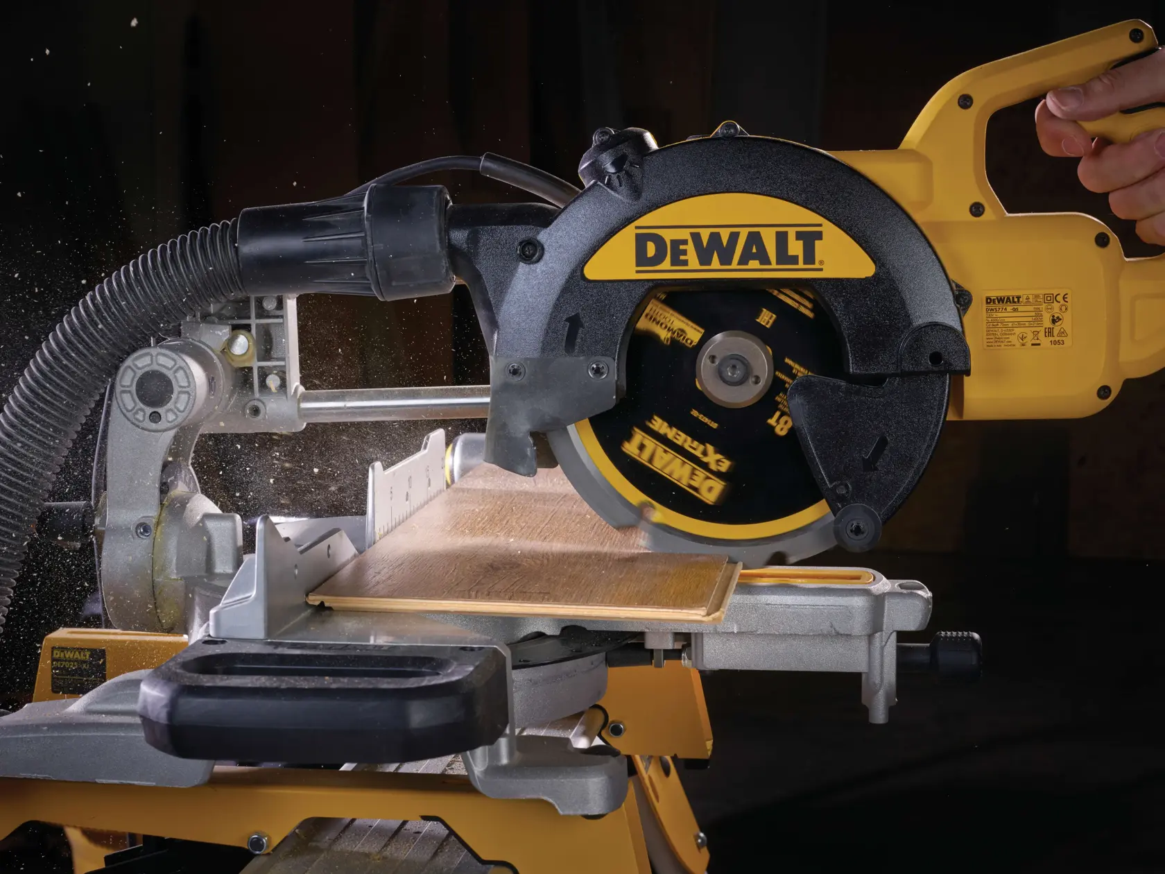 DEWALT circular saw cutting wood, close-up view with dust extraction hose attached, blade in action.