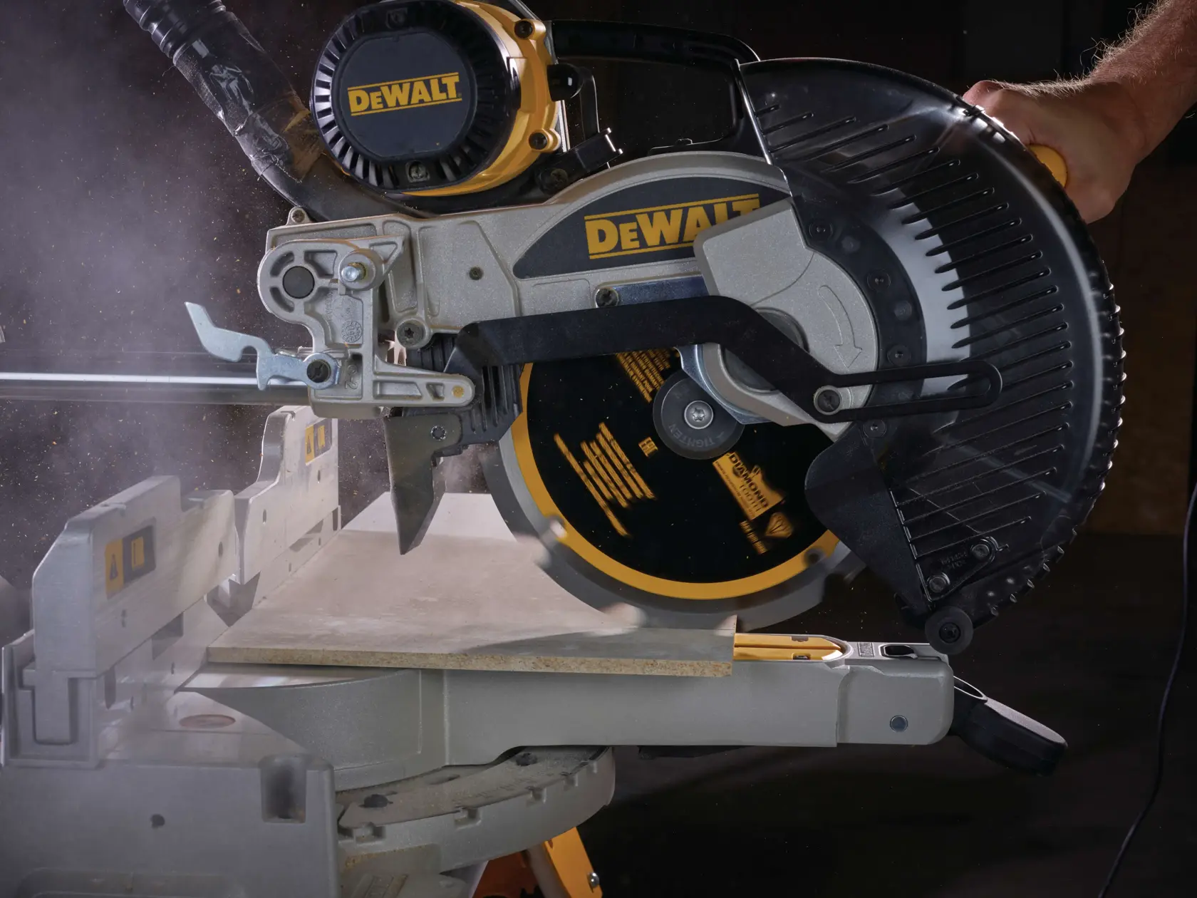 A DEWALT miter saw cutting a board, with visible dust and motion during operation.