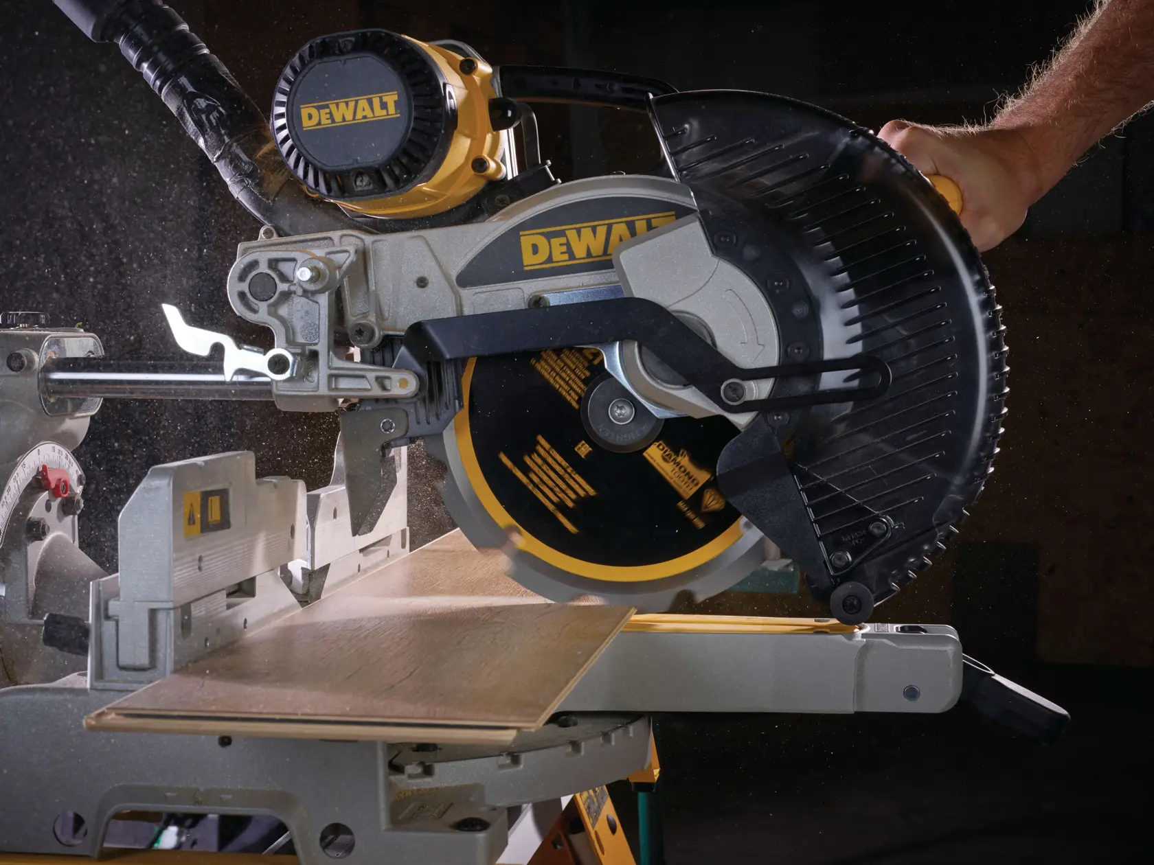 DEWALT miter saw cutting wooden plank, close-up view, dust particles visible during operation.