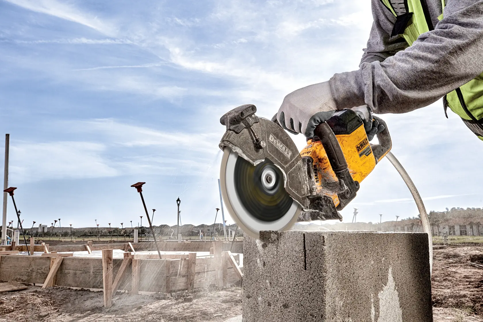 DEWALT DT20462-QZ, DT20462 power saw cutting concrete block outdoors, worn by gloved hand. Photography product.