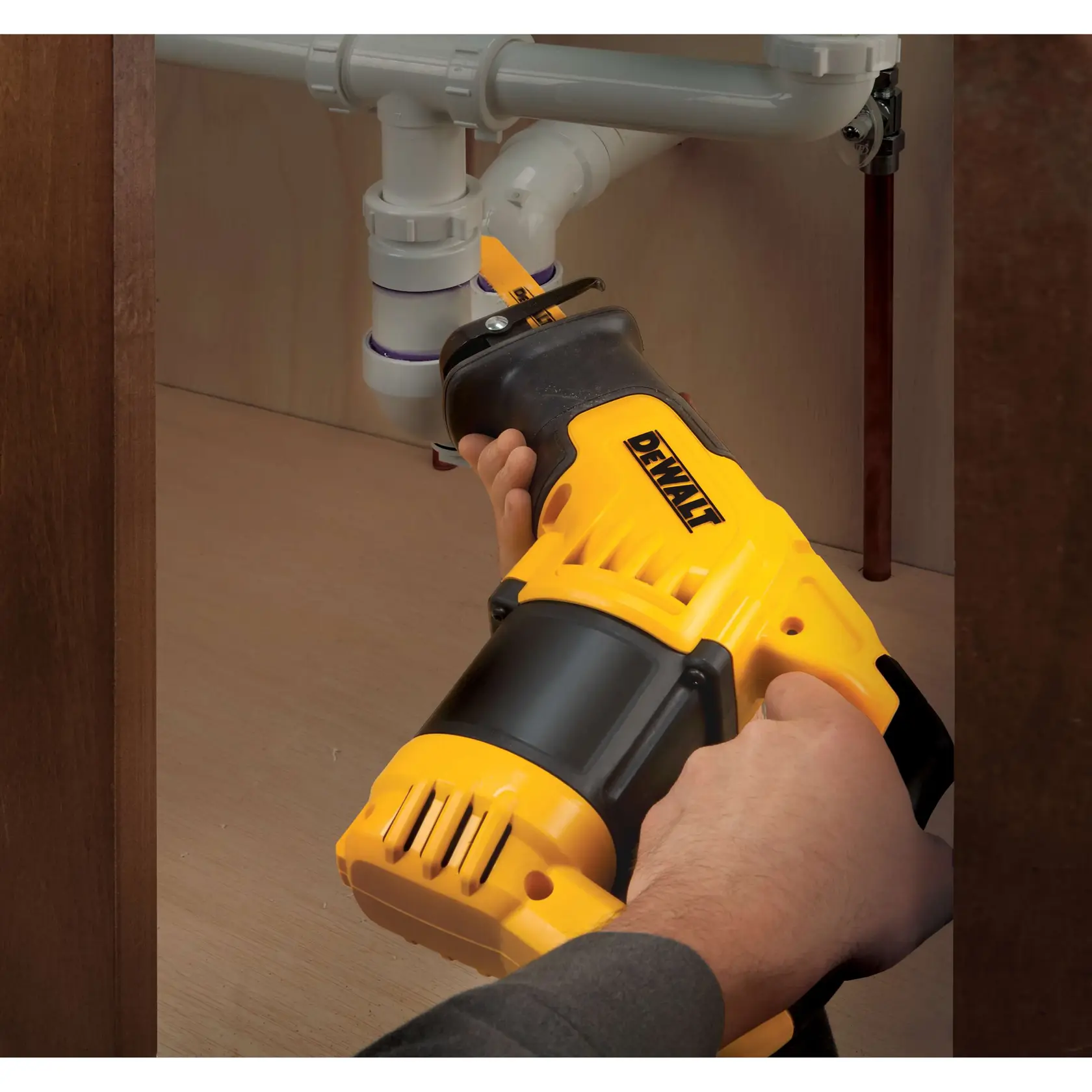 Person using a DEWALT reciprocating saw to cut pipes under a sink in a cabinet.
