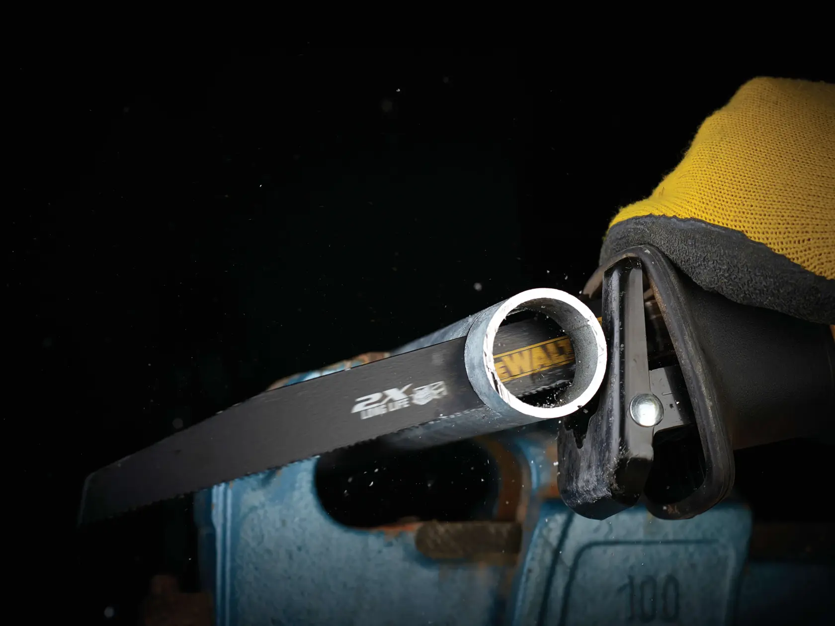 DEWALT saw blade cuts through a metal pipe. Worker wears yellow gloves for safety.