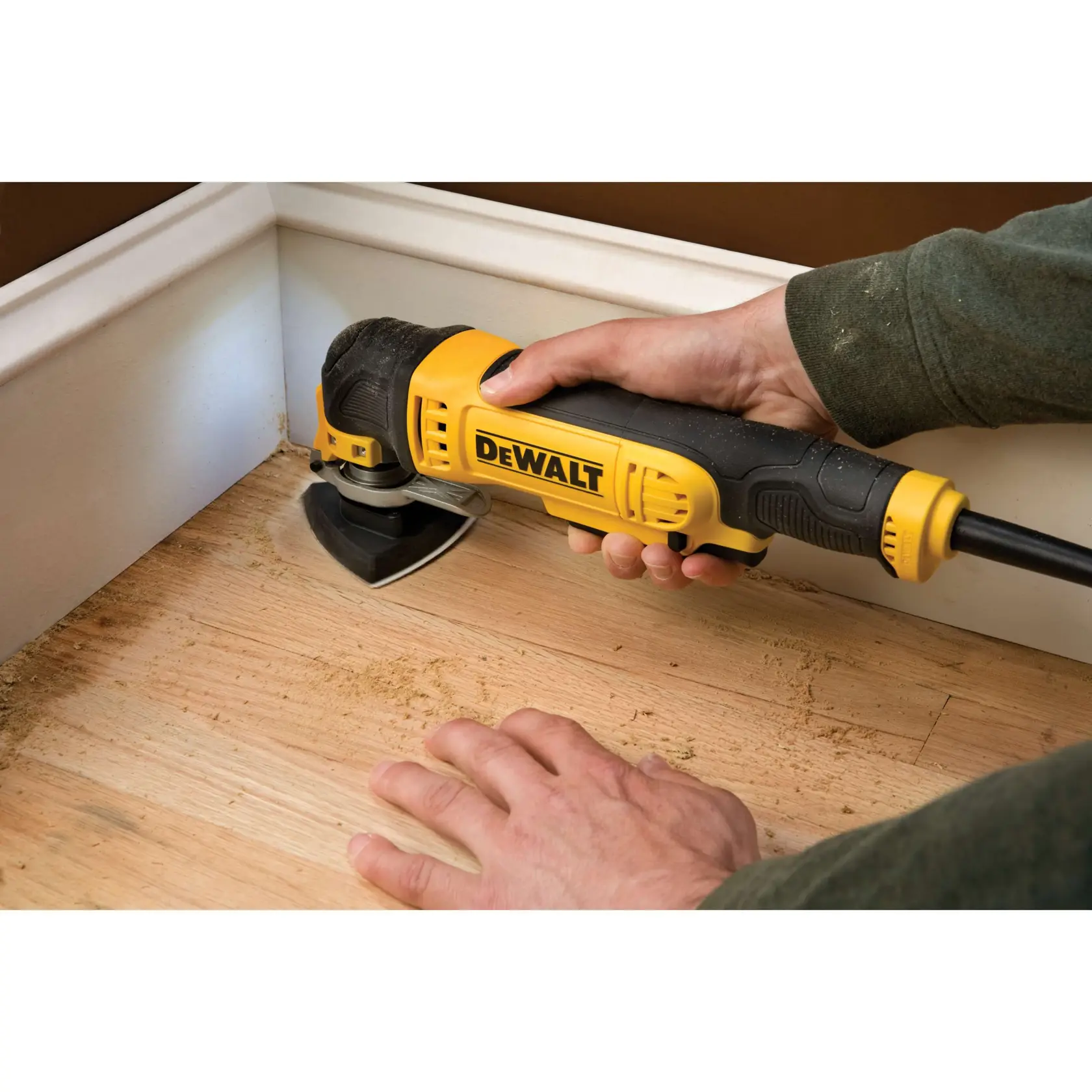 DEWALT tool sanding wood floor near wall corner, held by person in green sleeve.