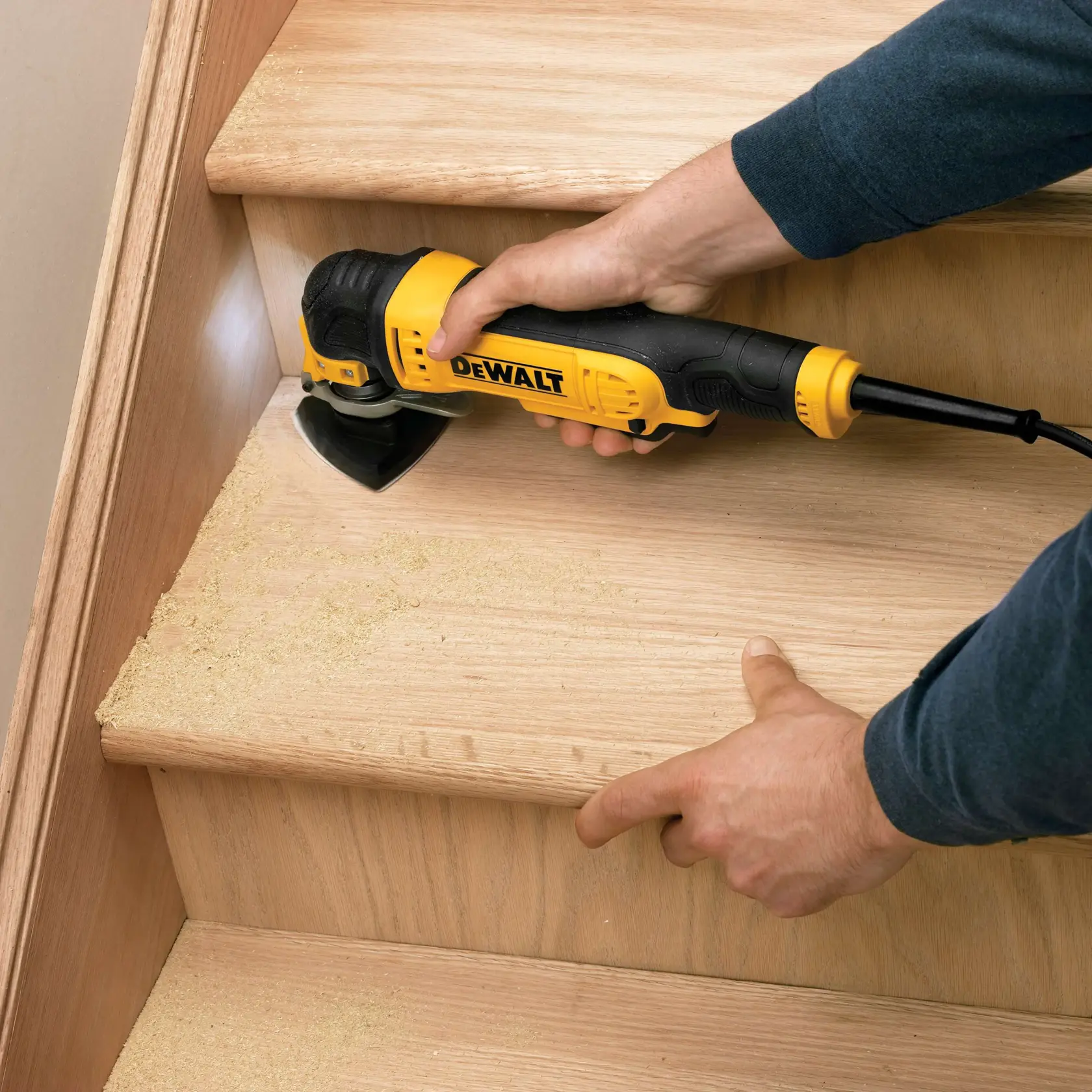 A DEWALT sander is being used on a wooden staircase, sanding the surface and creating sawdust.