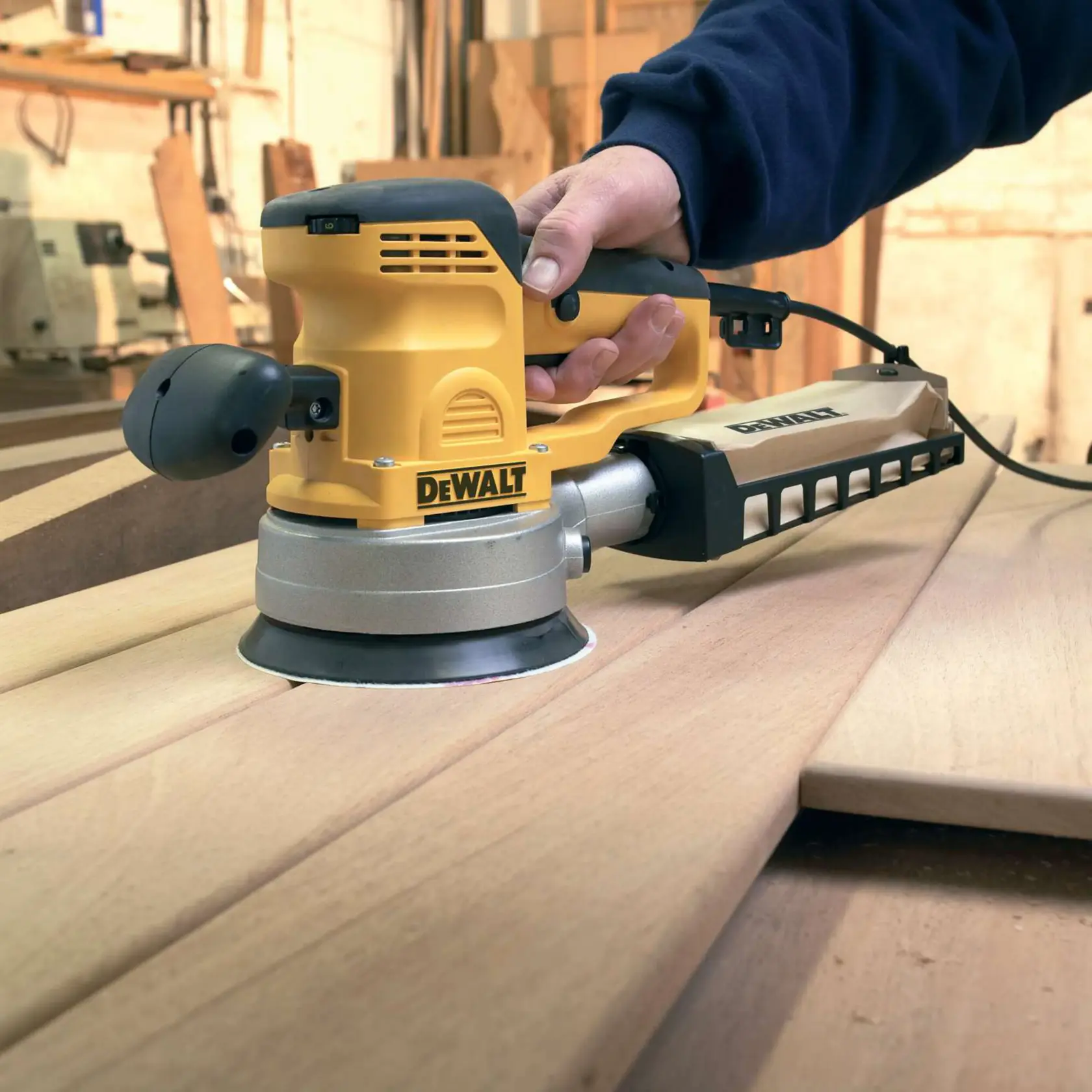 DEWALT sander in use on wooden boards in a workshop, held by a hand. Power tool for woodworking.