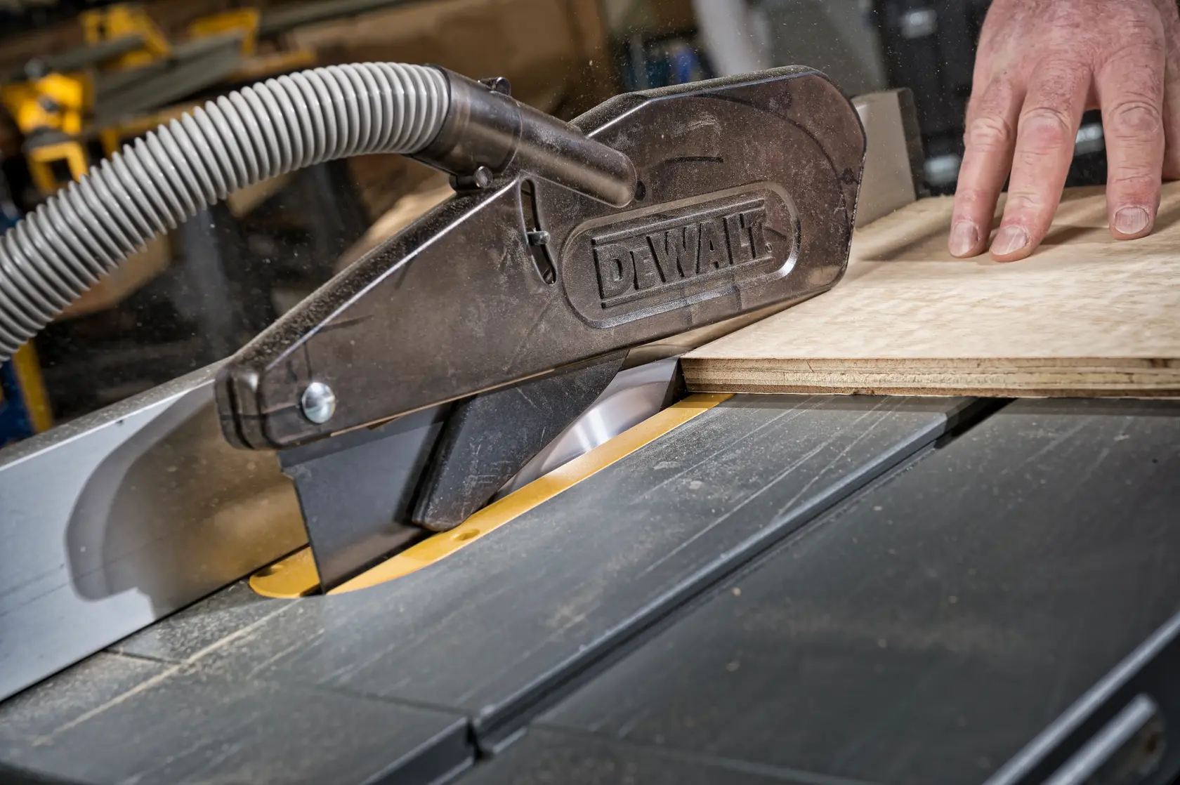 DEWALT table saw cutting wood, safety guard in place, close-up of hand and saw mechanism.