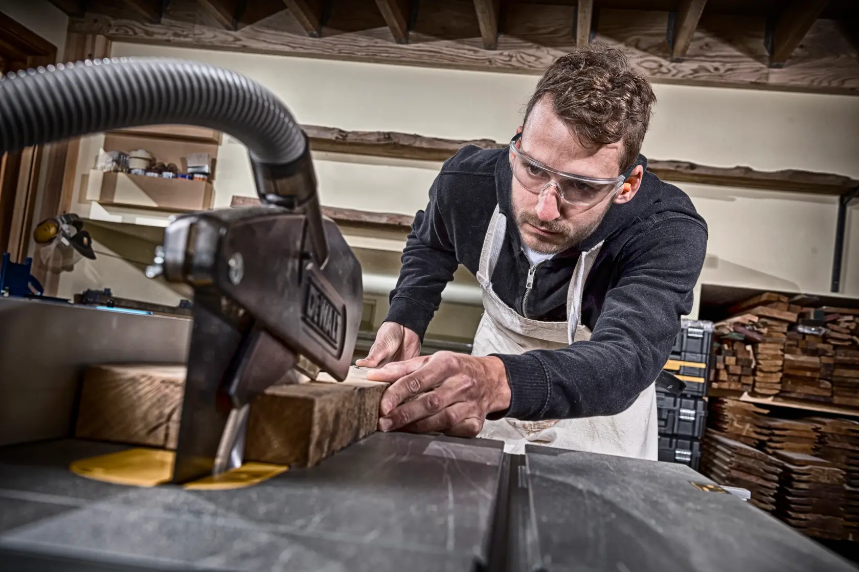 Person using a DEWALT machine to cut wooden planks in a workshop; face blurred for privacy.