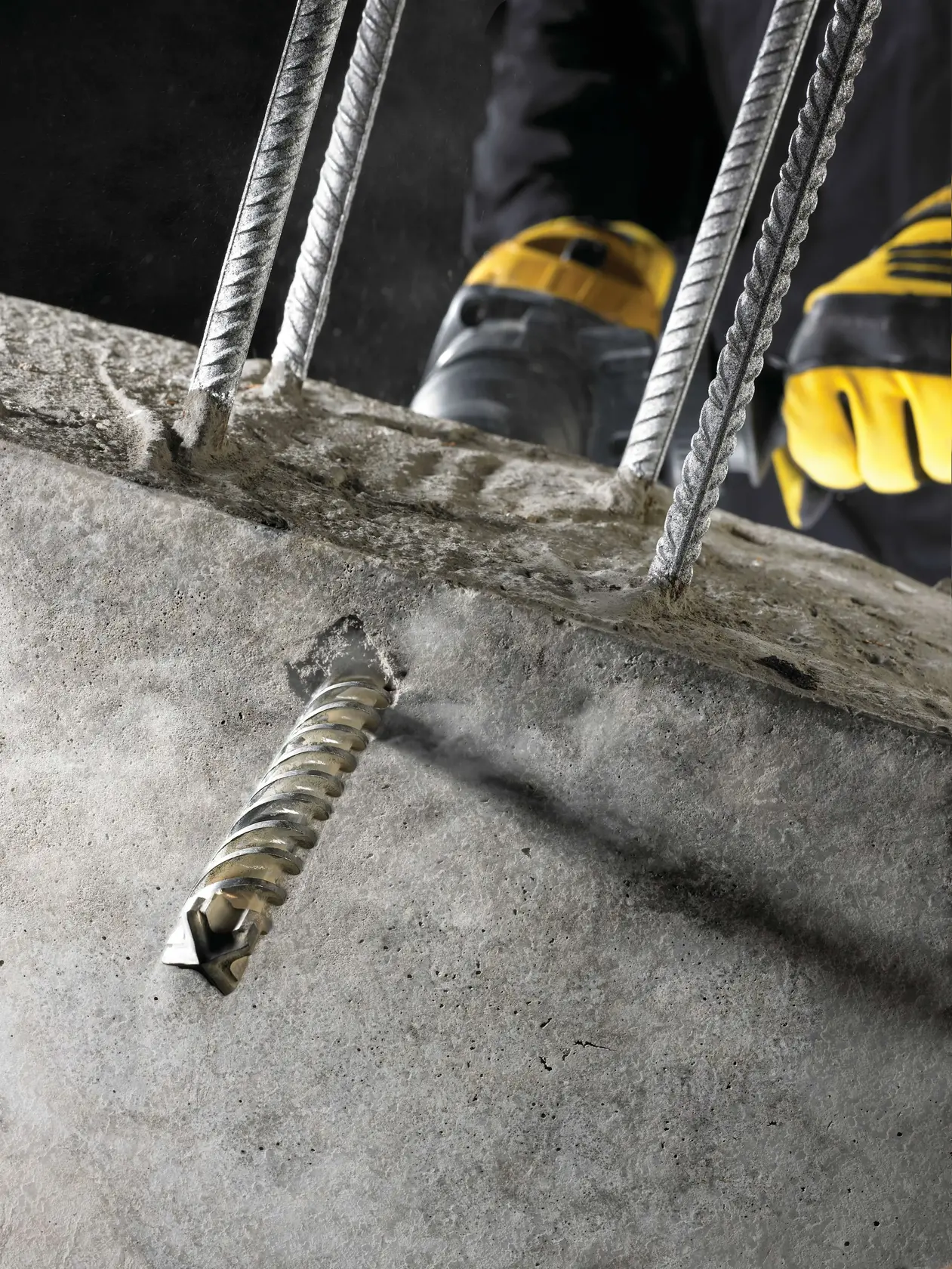 DEWALT DT60813 SDS-Plus drill bit in concrete near rebar, worker with yellow gloves in background, close-up photo.