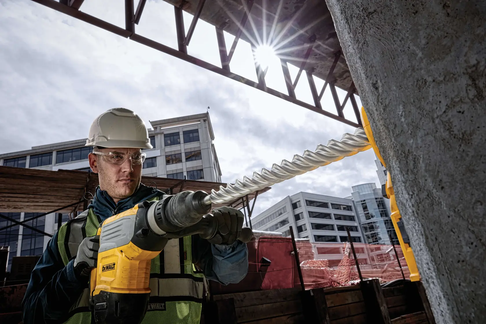 Photo of worker using DEWALT DT60838 rotary hammer drill on concrete at construction site in daylight.