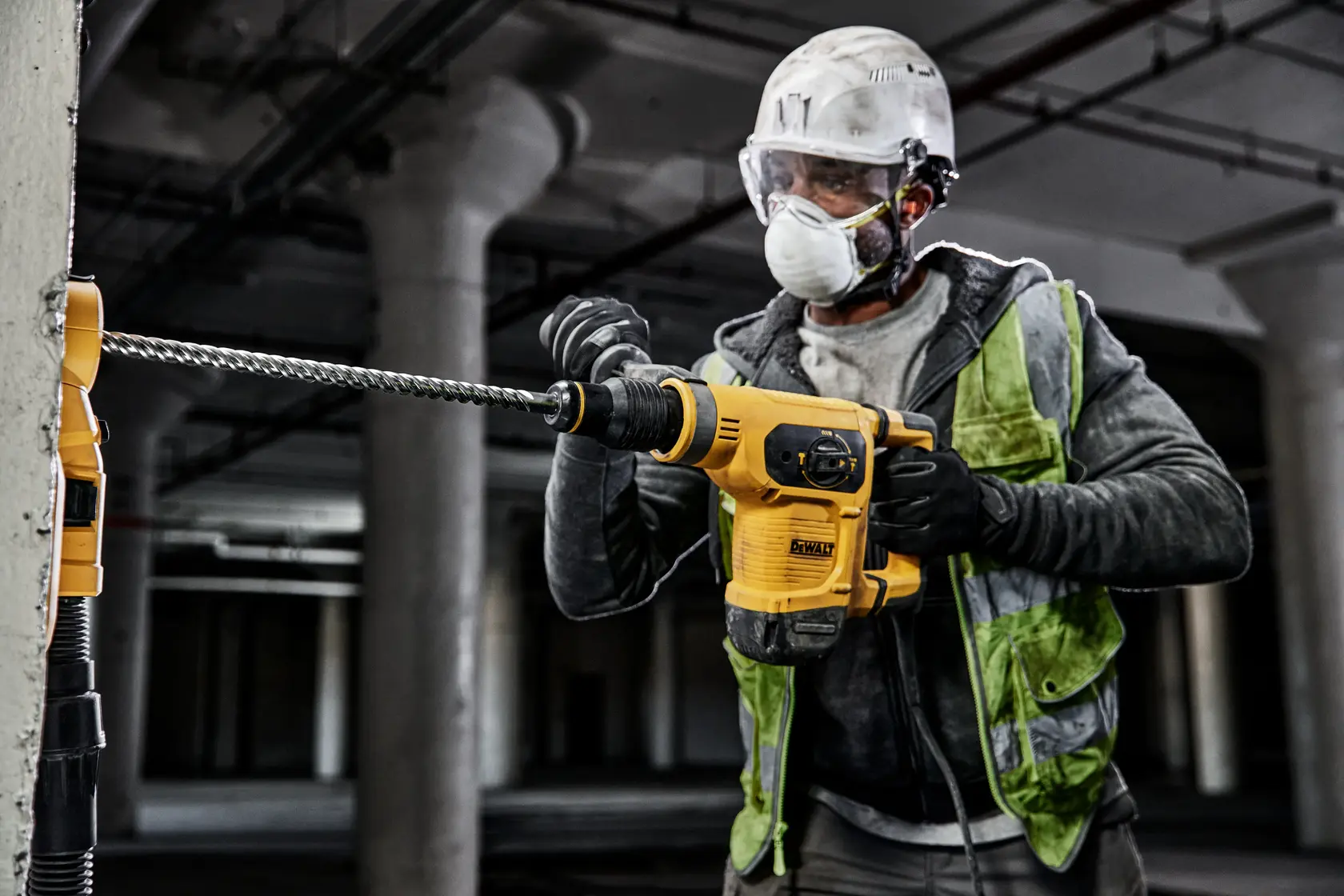 Photo of worker using DEWALT DT60839 rotary hammer drill on concrete wall, wearing safety gear.