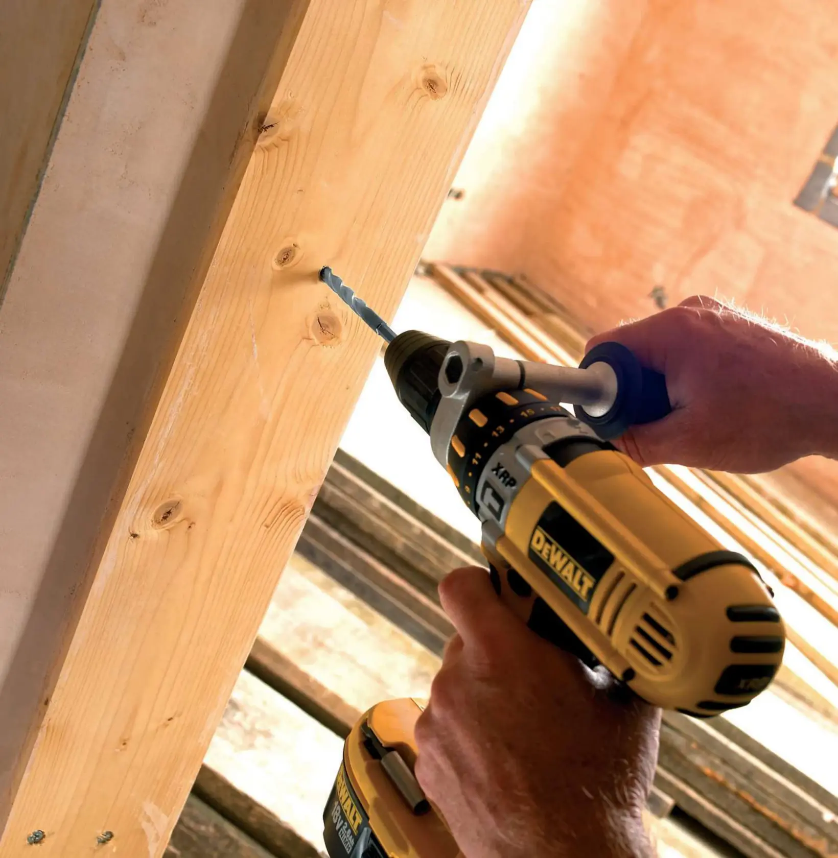 Person using a DEWALT drill to bore a hole in a wooden beam at a construction site.