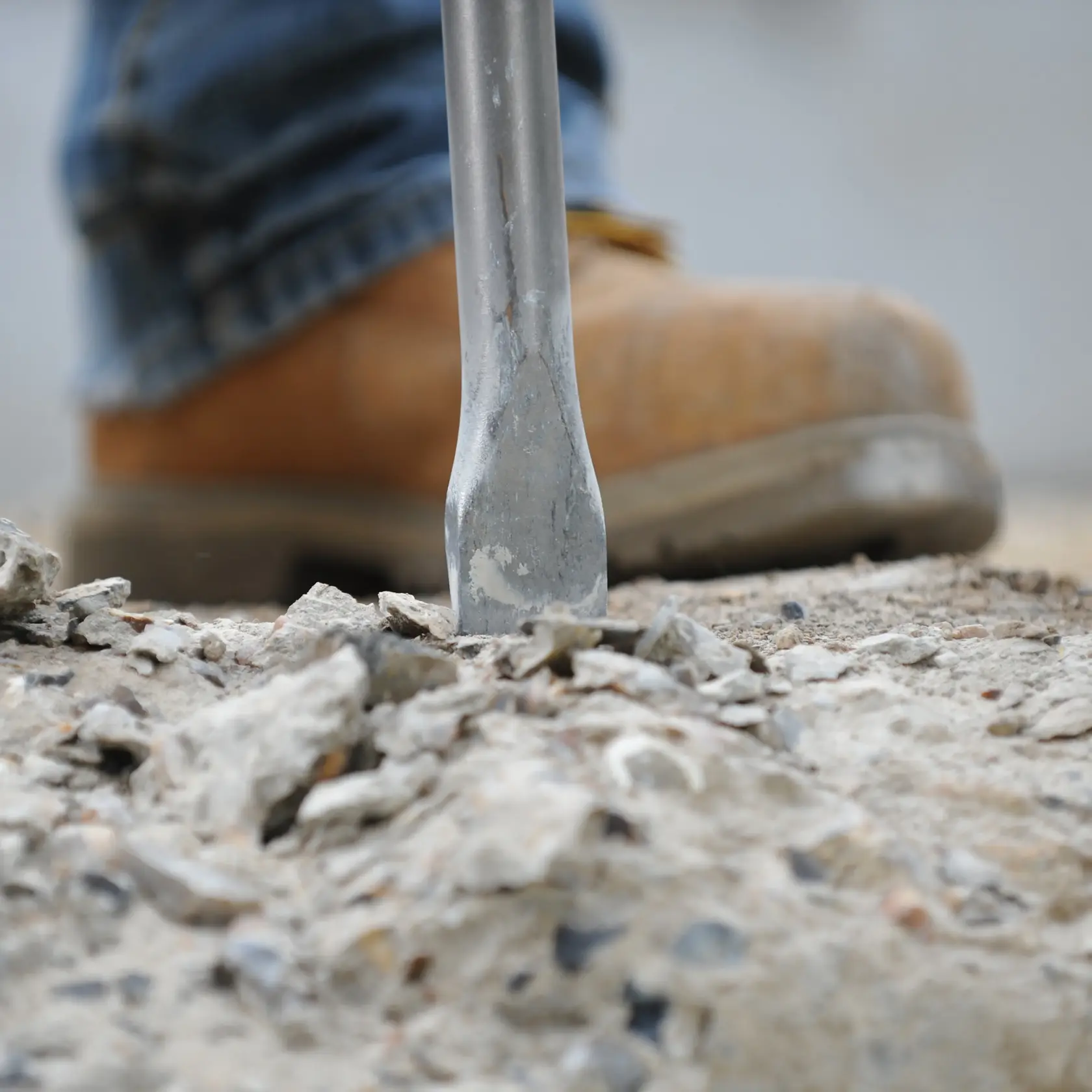 Photo of DEWALT DT6802 chisel breaking concrete, worker boot in background, product close-up.