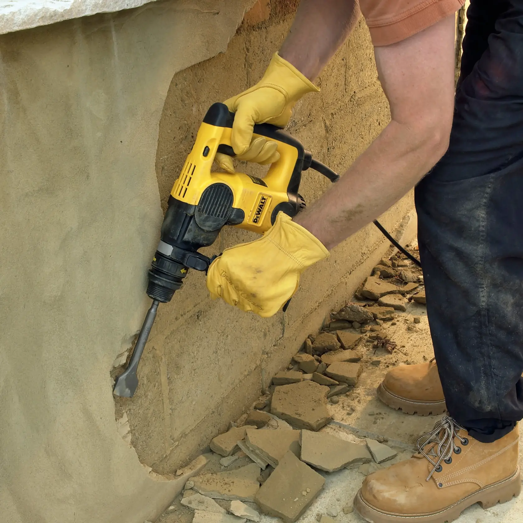 Photo of DEWALT DT6803 chisel in use on concrete wall by worker wearing yellow gloves and boots.