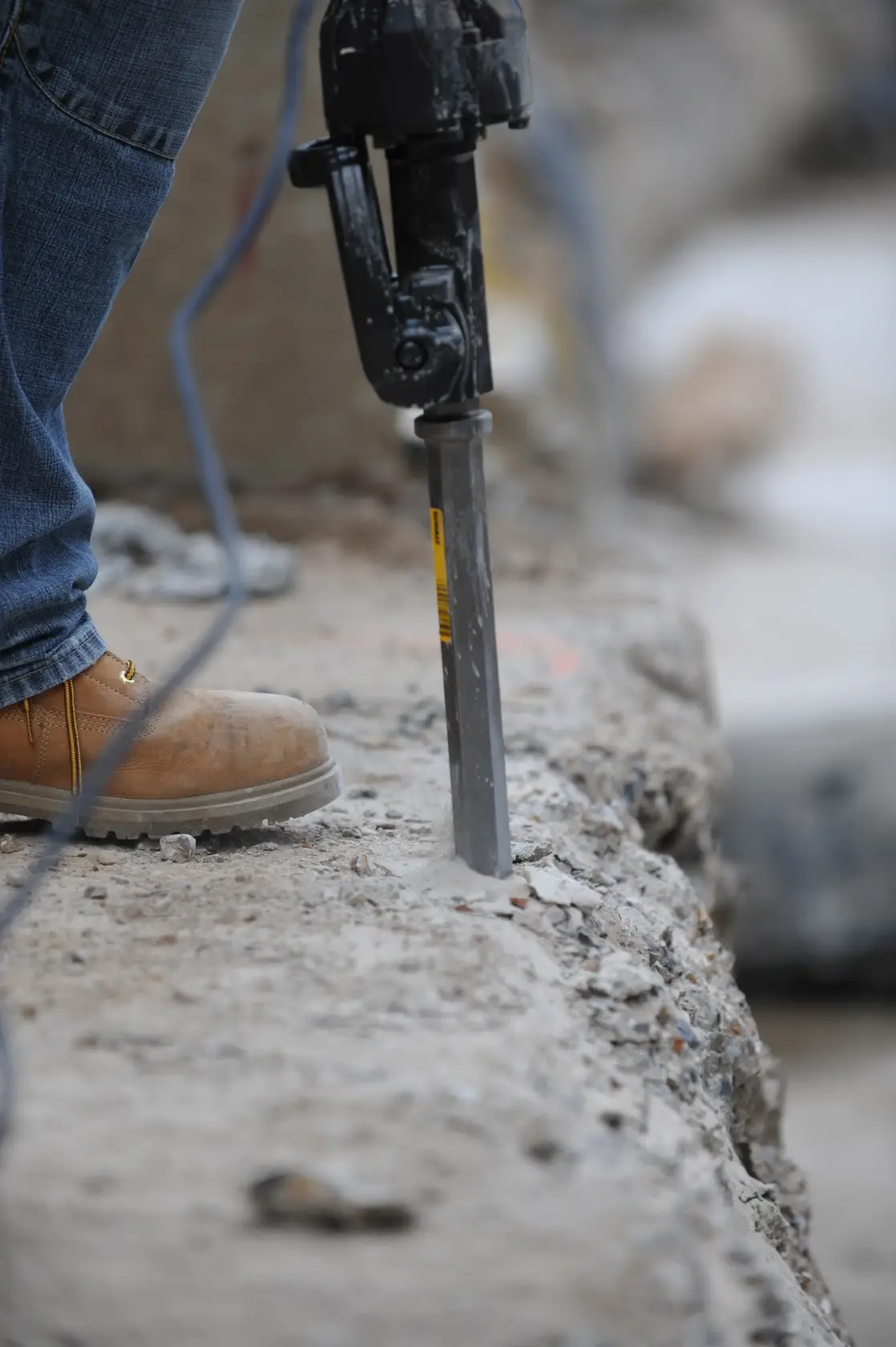 DEWALT DT6929-QZ, DT6929 chisel in use, worker breaking concrete, close-up, construction site, boots visible.