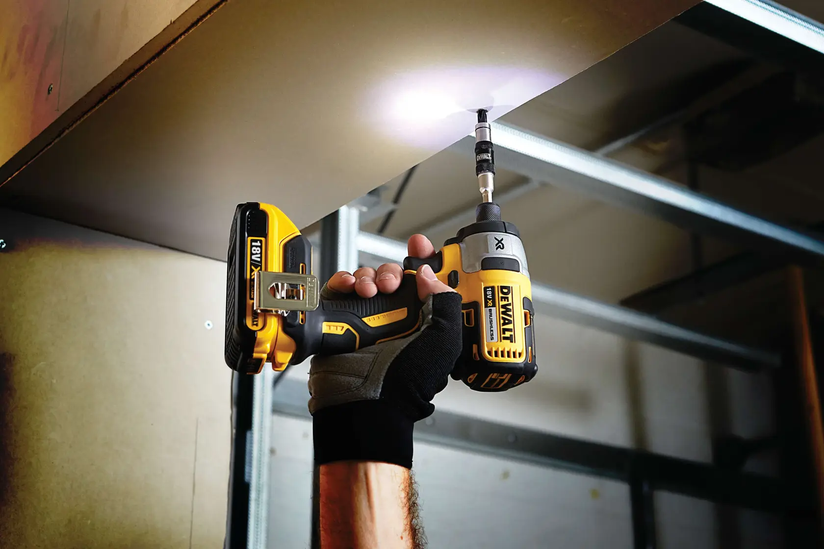 Photo of DEWALT impact driver DT70518T used to drive screw overhead, glove on hand, indoor workspace.