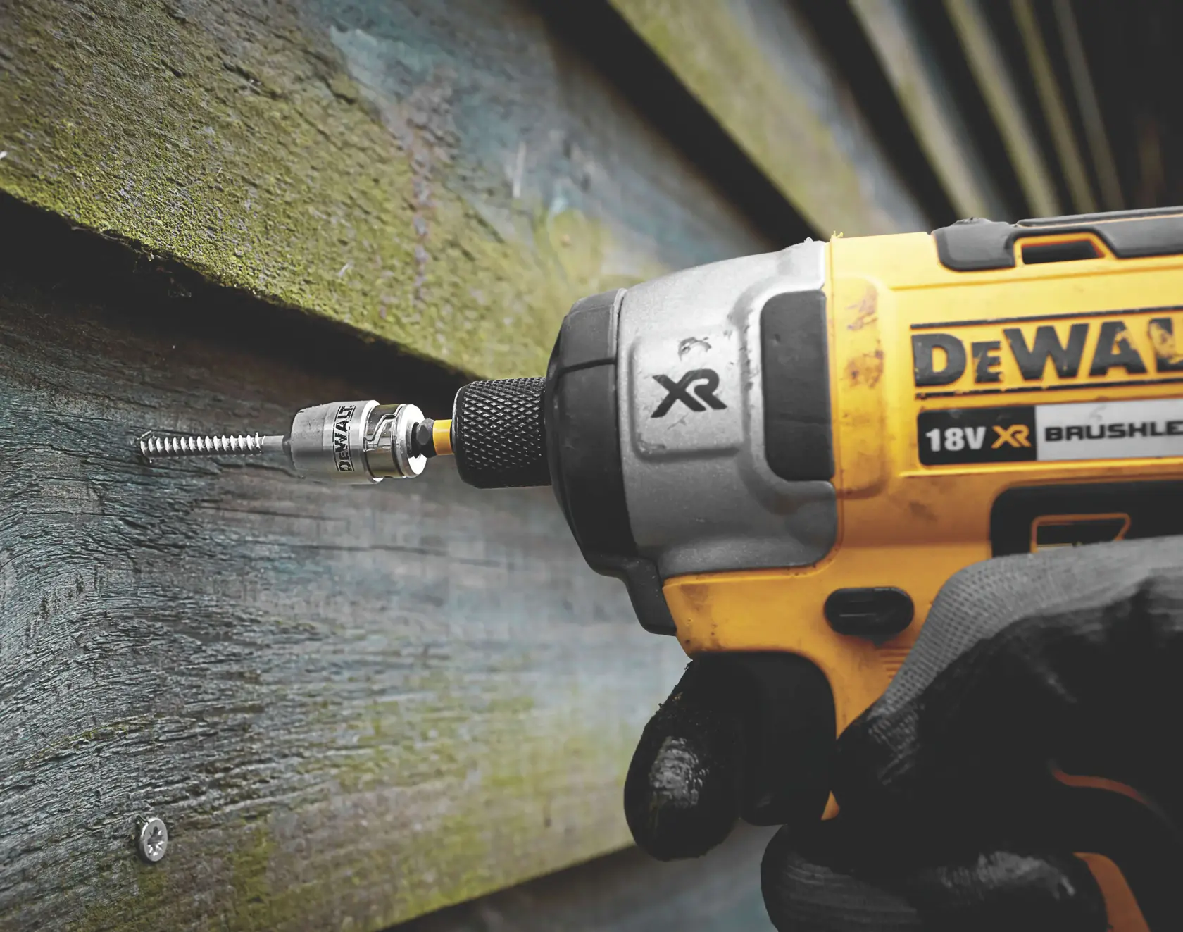 DEWALT impact driver with bit driving a screw into outdoor wood siding.