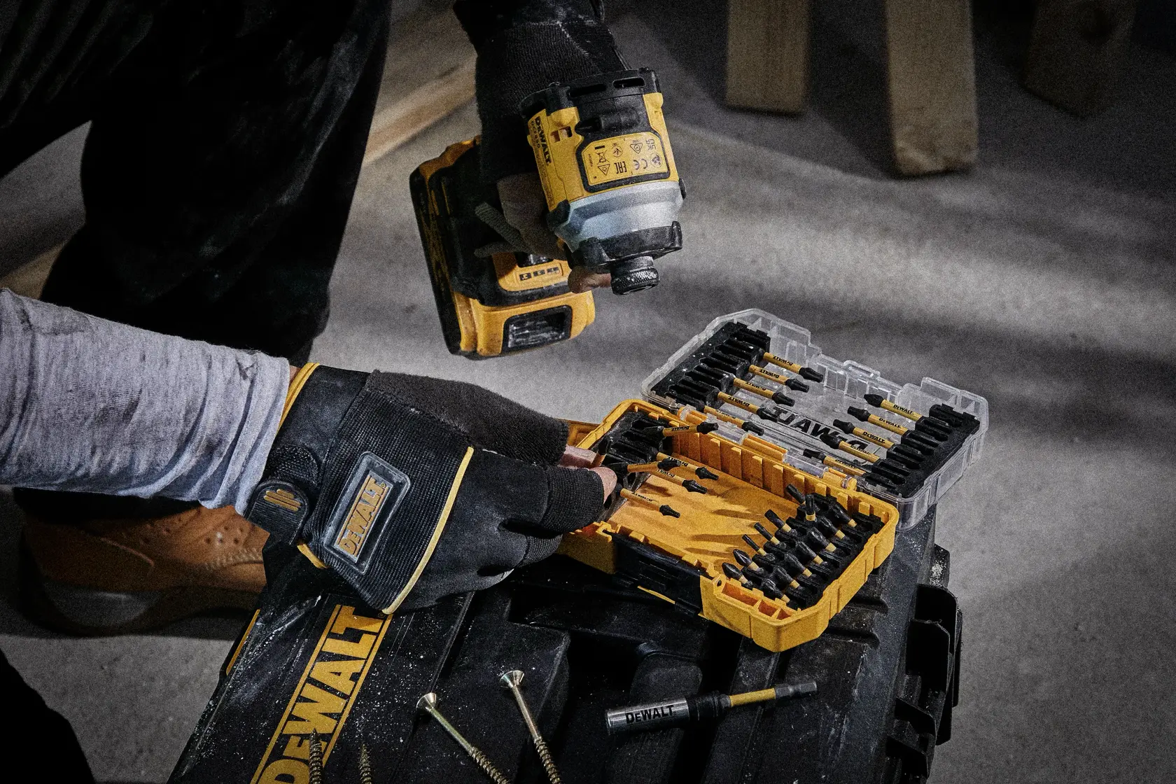 Person wearing gloves uses a DEWALT drill and opens a DEWALT drill bit set case on a toolbox in a workshop.